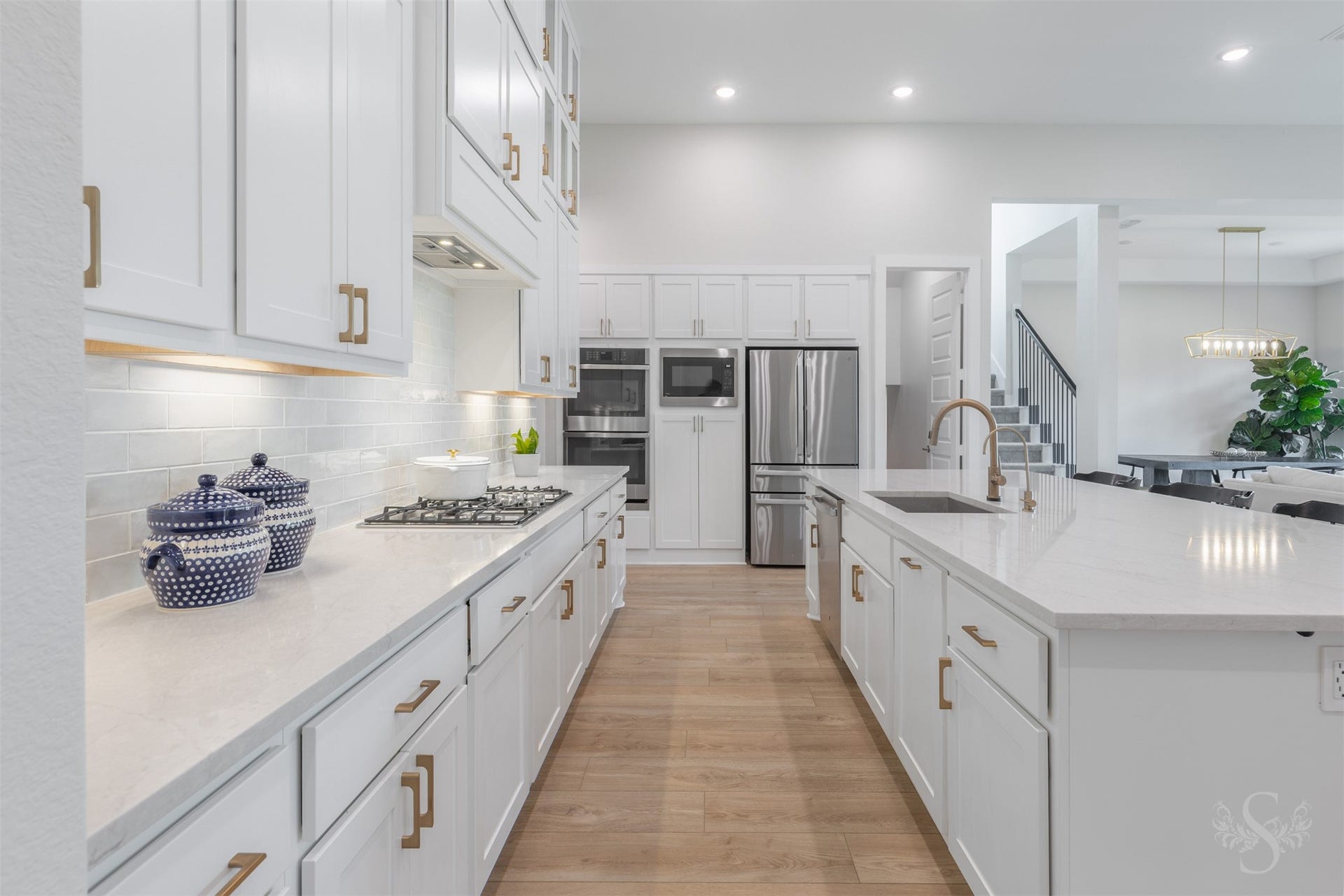 Beautiful white cabinetry offers an exceptional amount of storage, complemented by quartz counters and an elegant tile backsplash. Under-cabinet lighting beautifully highlights the backsplash and warm gold hardware.