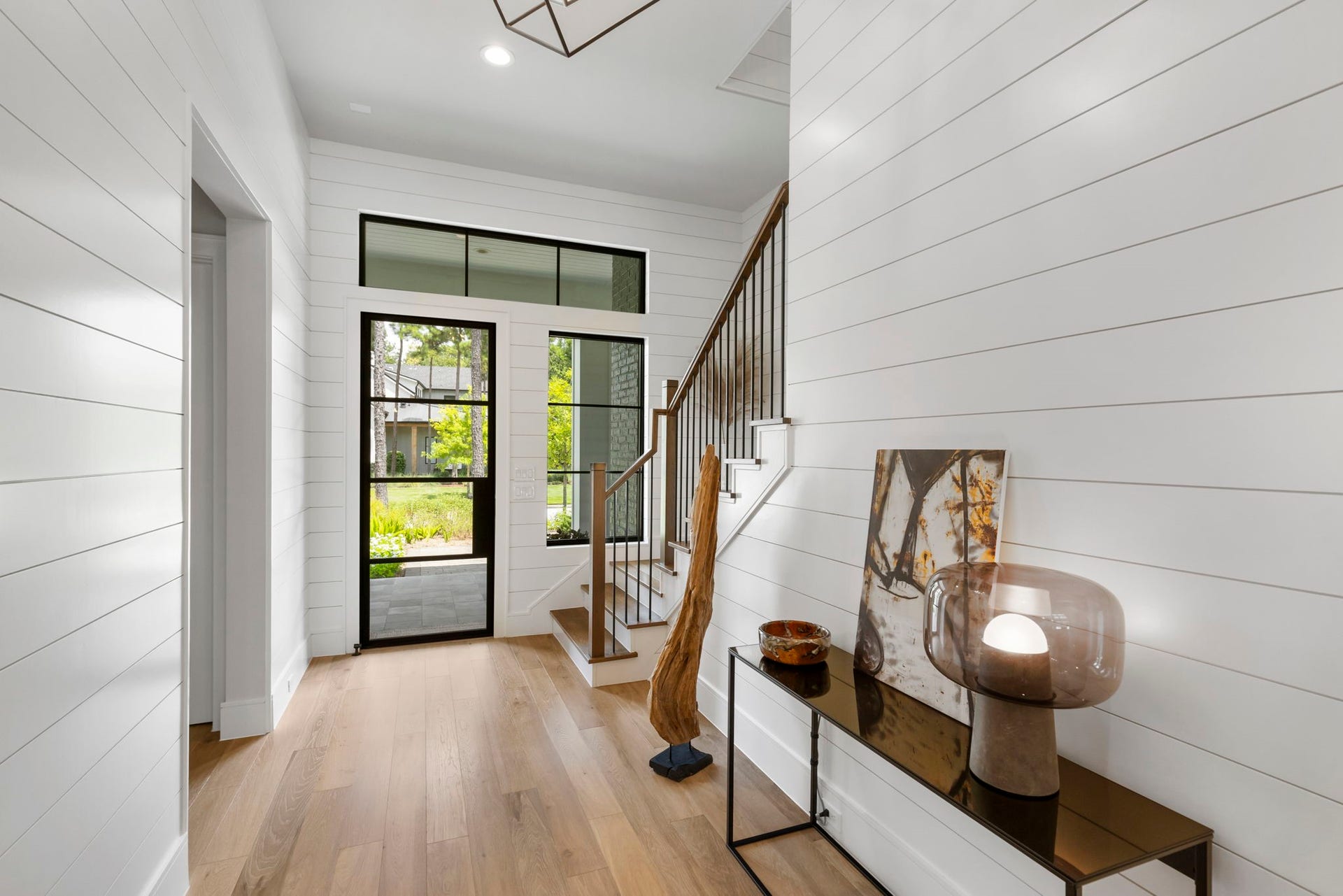 A modern style black steel front door is flanked by a sidelight and topped with a full transom, bringing in abundant natural light and views of the front landscaping