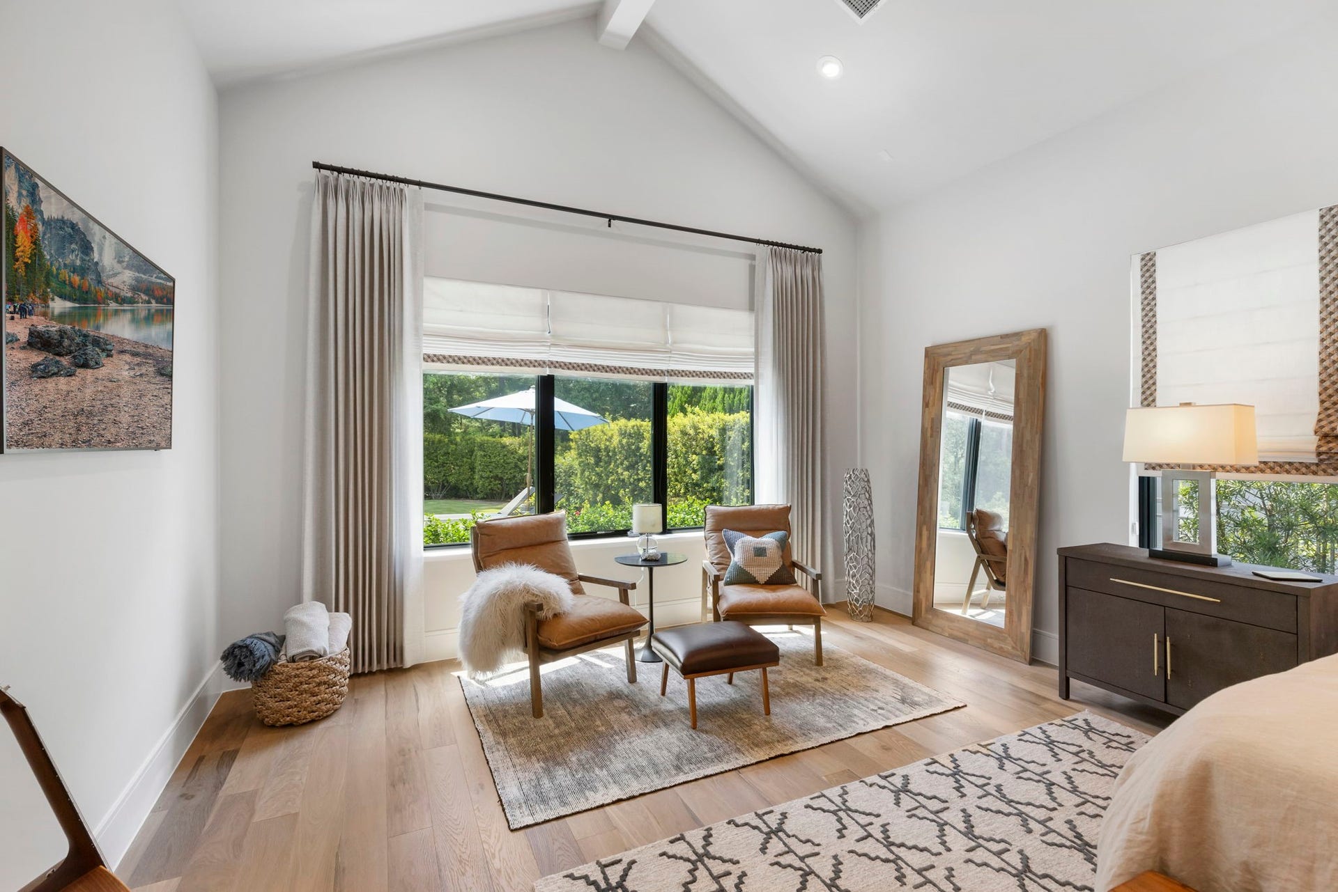 Upon entering the primary bedroom, to the left is a cozy sitting area overlooking the backyard through oversized windows, framed by a vaulted ceiling.