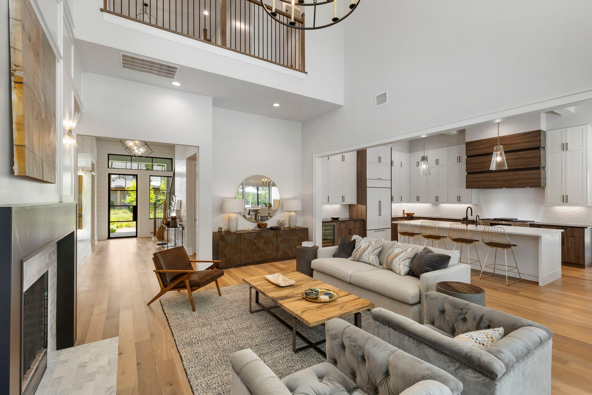 This open-concept living space seamlessly connects the living room, kitchen, and entry, all beneath dramatic two-story ceilings and an overlooking loft.