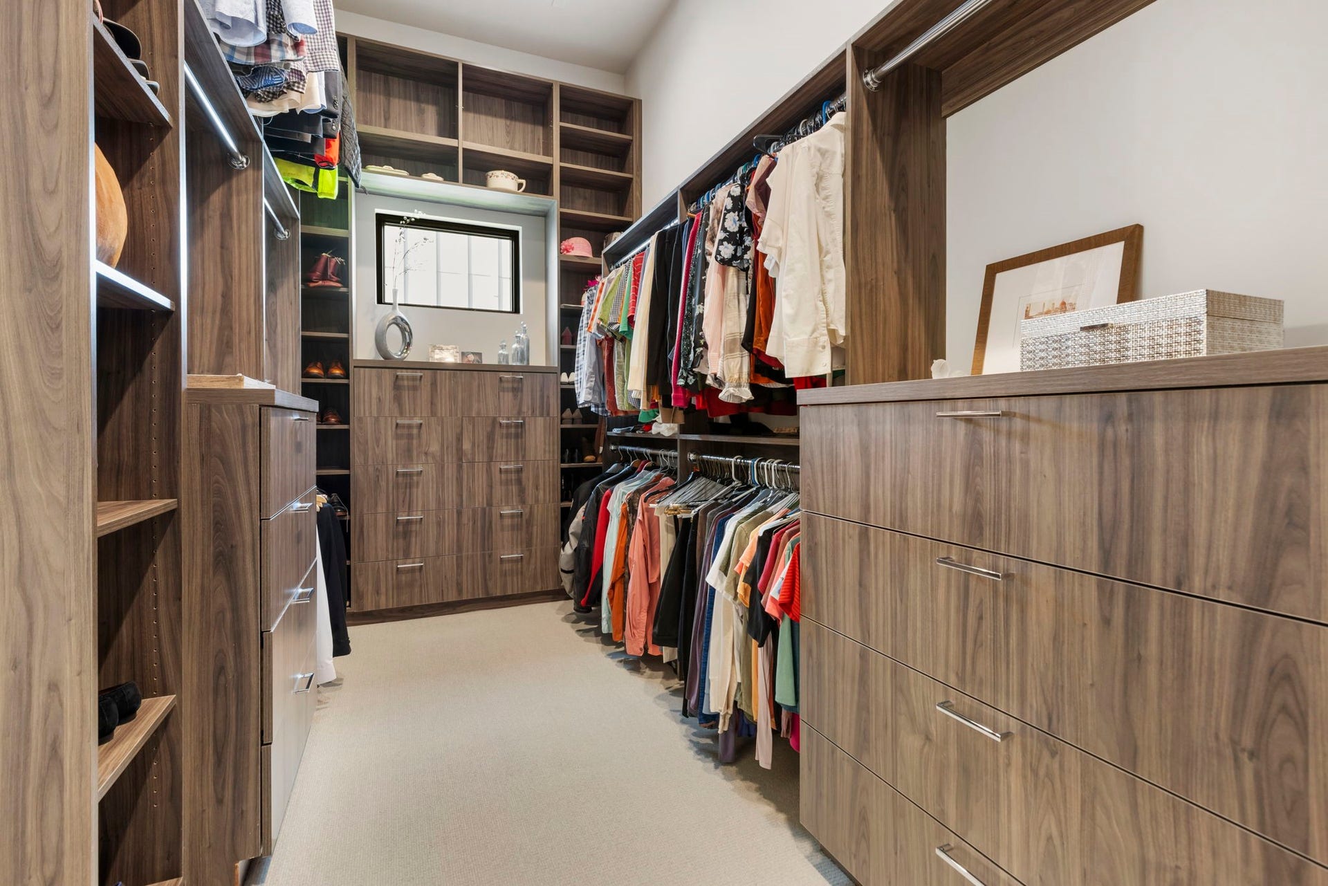 Primary closet impresses with floor-to-ceiling custom built-ins, offering exceptional storage with double hanging rods, drawers, and display shelving.
