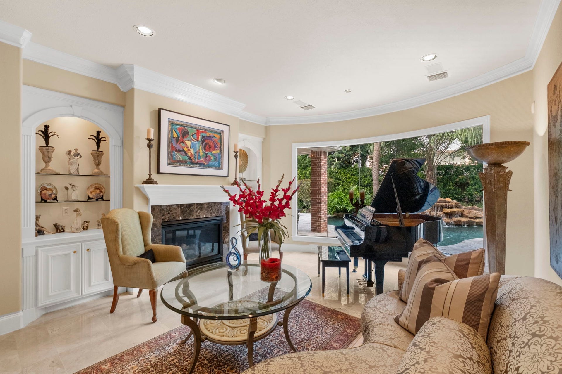 7 Silverloch Court, Sugar Land, TX 77479 Elegant living room features a cozy gas log fireplace built-in shelving overlooking a lush backyard with a pool. Luxurious seating areas create an inviting ambiance.