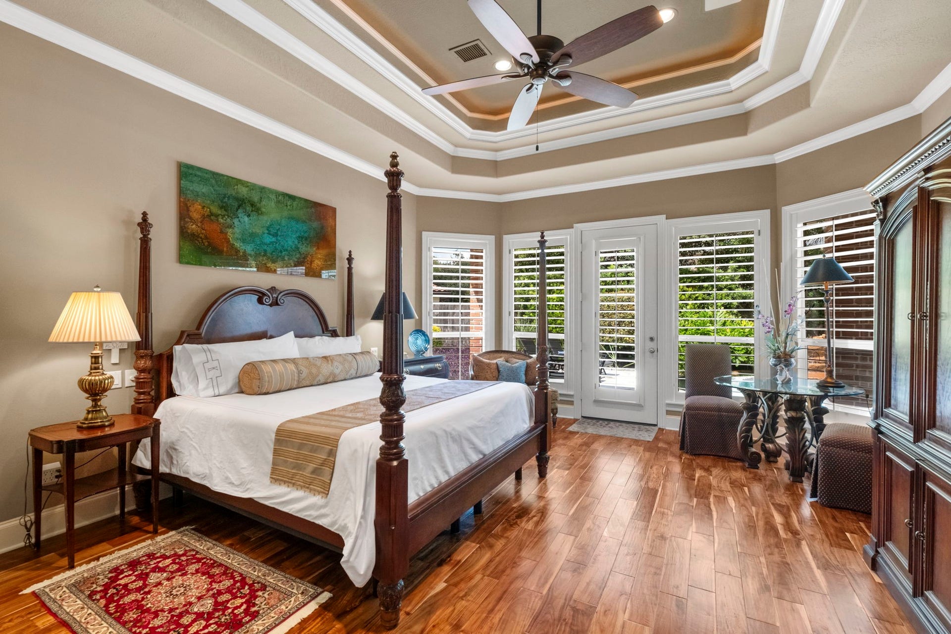 7 Silverloch Court, Sugar Land, TX 77479 Elegant master bedroom featuring a tray ceiling, rich acacia hardwood floors, and abundant natural light from large windows with plantation shutters. There is a door leading to the backyard so you can slip out and enjoy a dip in the pool first thing in the morning or right before you hop in bed at night.
