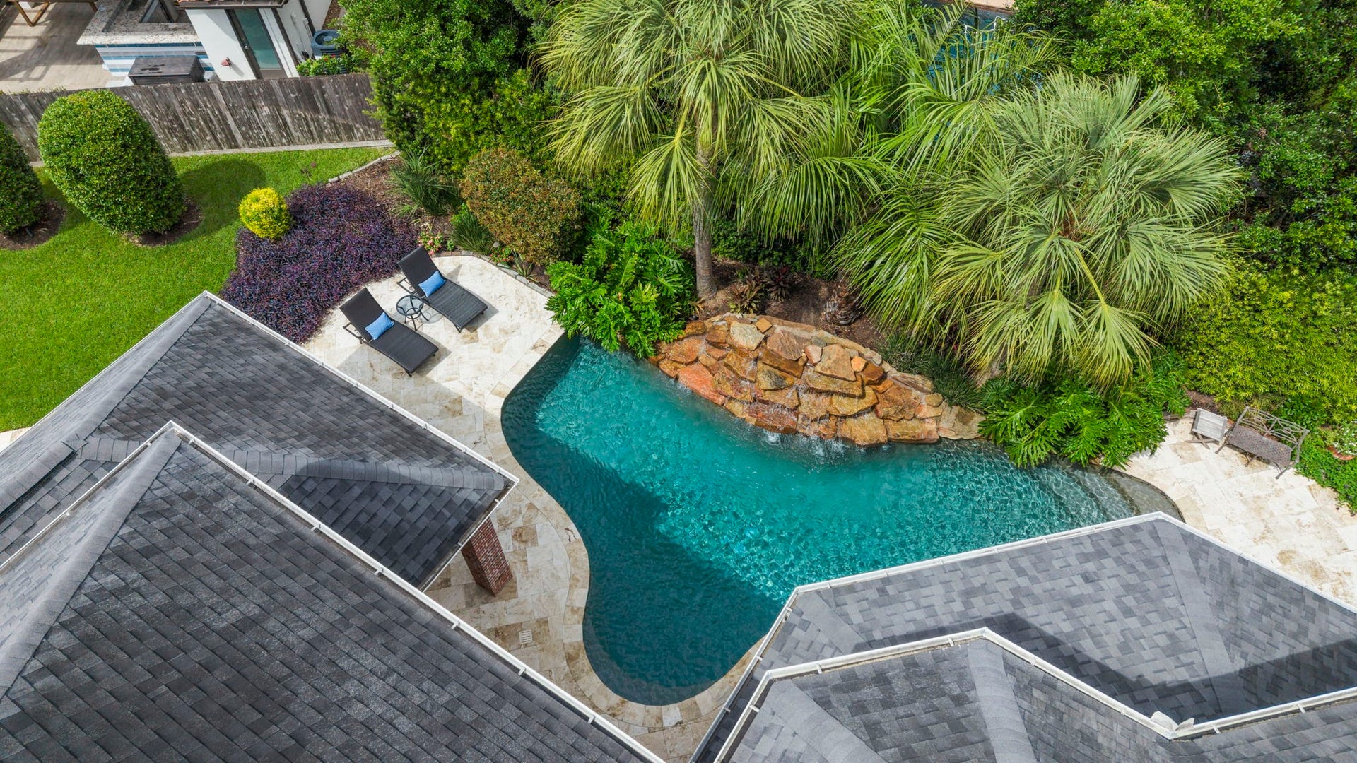 7 Silverloch Court, Sugar Land, TX 77479 Luxurious backyard oasis featuring a sparkling pool with a natural rock waterfall, surrounded by lush landscaping and ample space for relaxation.