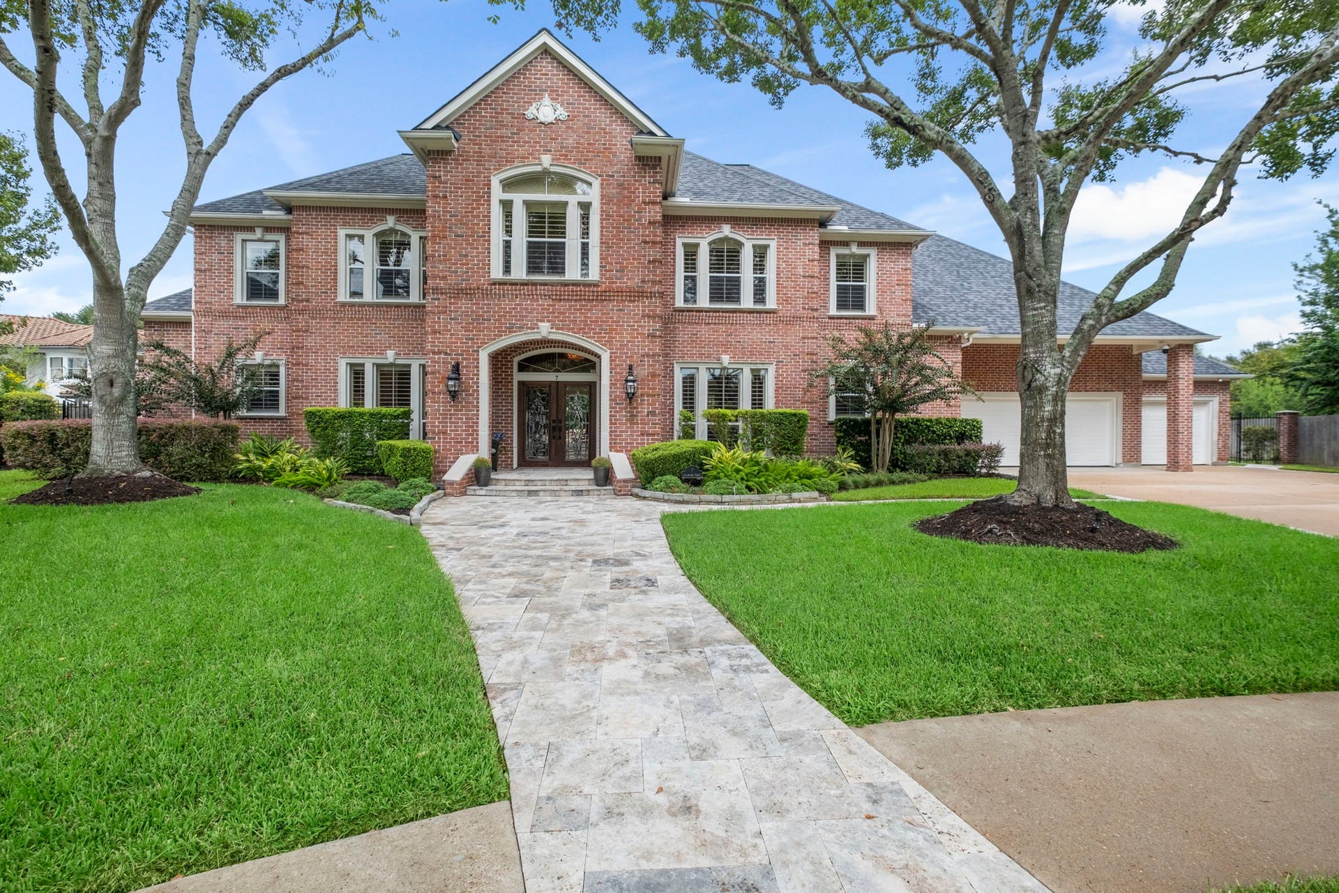 7 Silverloch Court, Sugar Land, TX 77479 Stunning brick colonial-style home with elegant curb appeal, featuring a beautifully landscaped front yard and a spacious driveway leading to a four and 1/2-car garage with an airconditioned workshop.