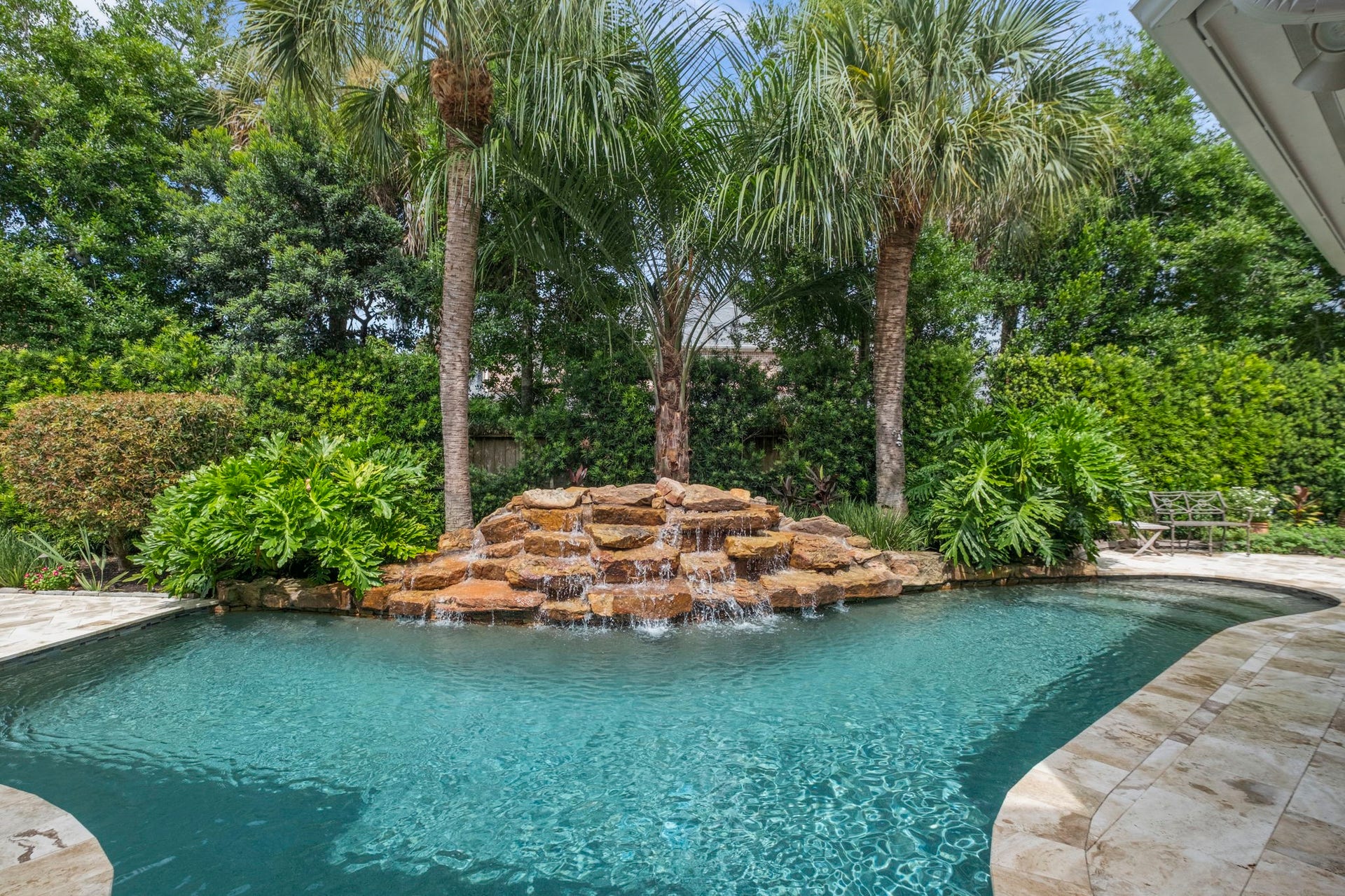 7 Silverloch Court, Sugar Land, TX 77479 Experience tropical serenity in this lush backyard oasis, featuring a sparkling pool with a cascading waterfall and surrounded by vibrant greenery and palm trees.