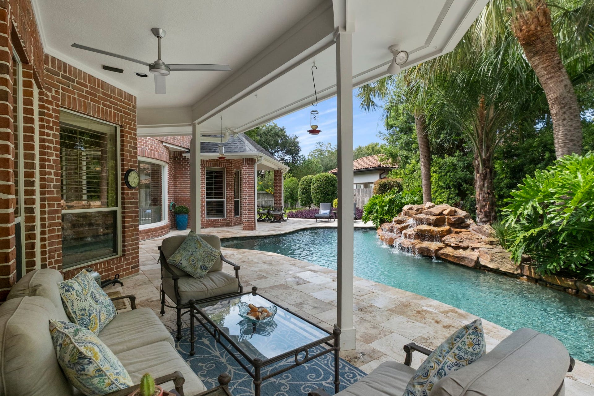 7 Silverloch Court, Sugar Land, TX 77479 Relax in this stunning outdoor oasis featuring a covered patio overlooking a sparkling pool with a waterfall feature, surrounded by lush landscaping and elegant brick architecture.