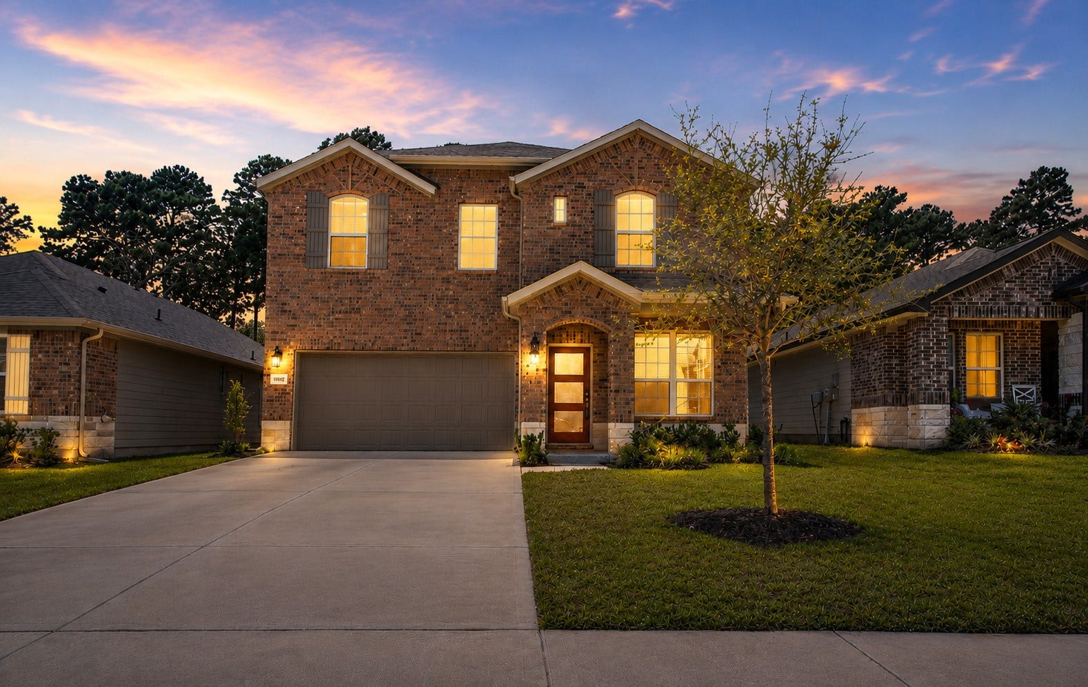 Striking two-story brick home with inviting curb appeal, a covered front entry, and beautifully illuminated landscaping.