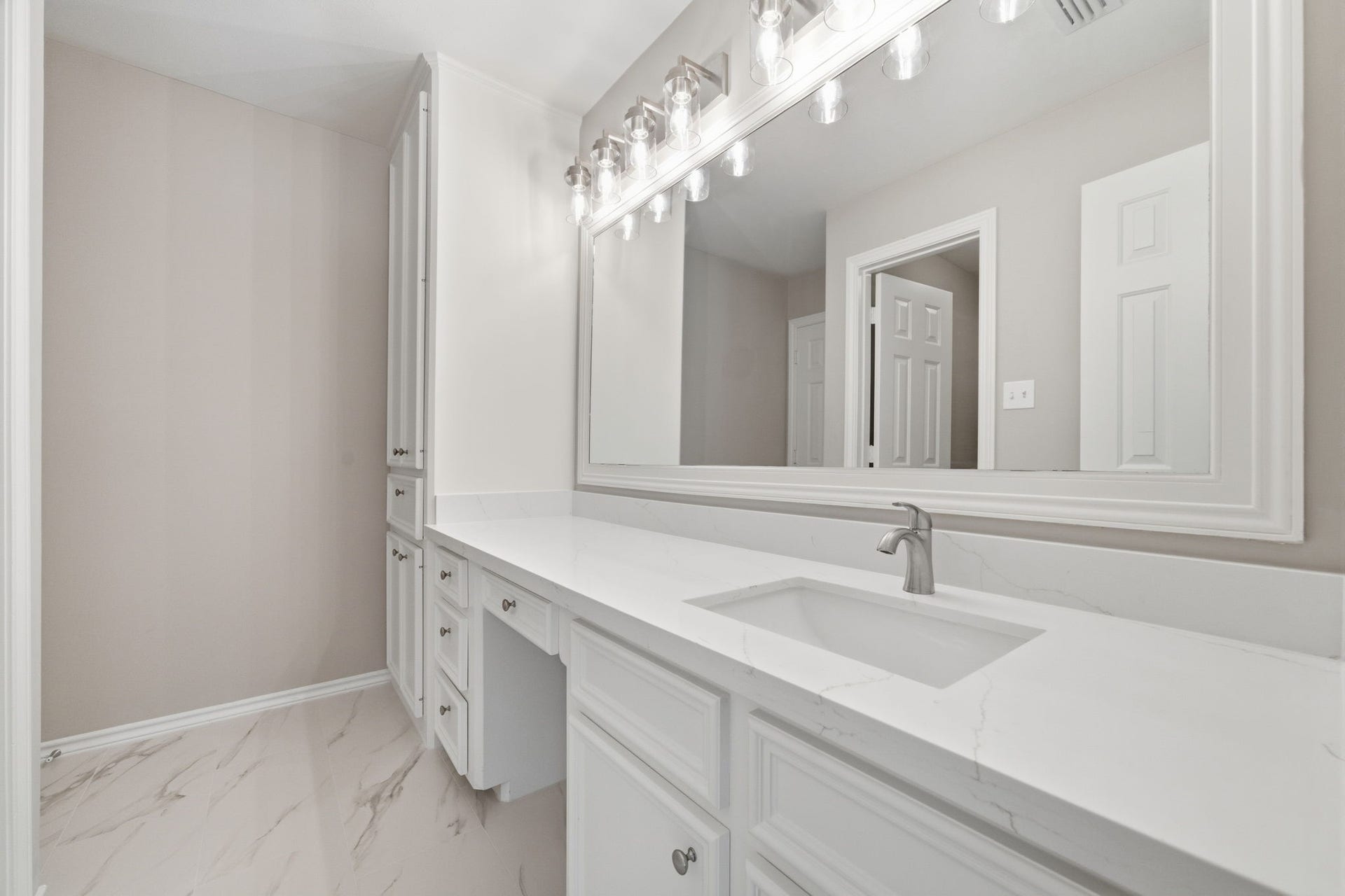 Renovated bathroom showcases a large mirror that visually expands the room while updated flooring gives the space a fresh, clean appearance.
