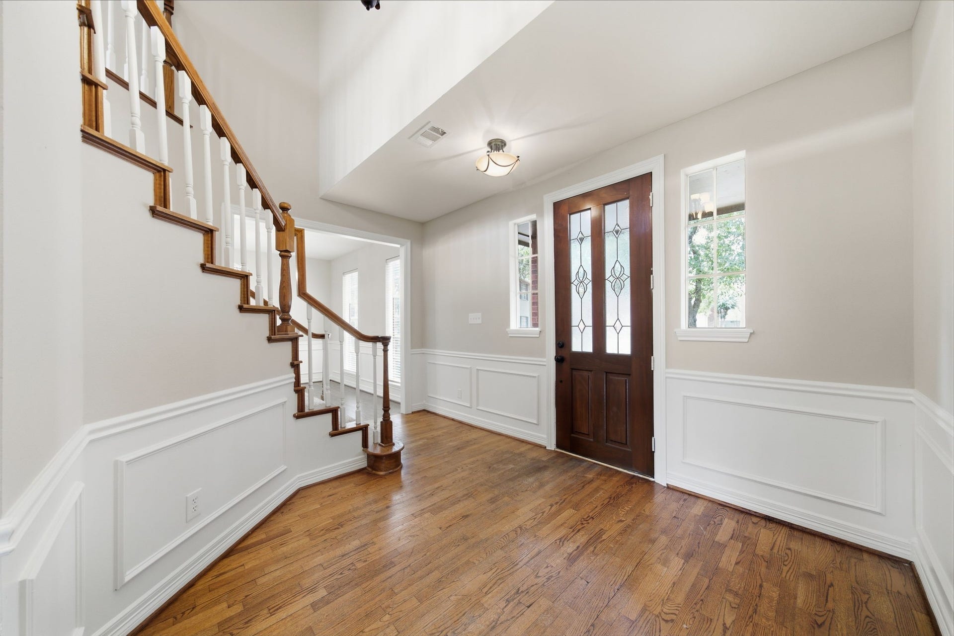 Elegant entryway featuring fresh paint, rich hardwood floors, a stunning wooden staircase with white accents, and a beautifully crafted front door with decorative glass panels, creating a warm and inviting first impression. Large storage closet under staircase with shelving!