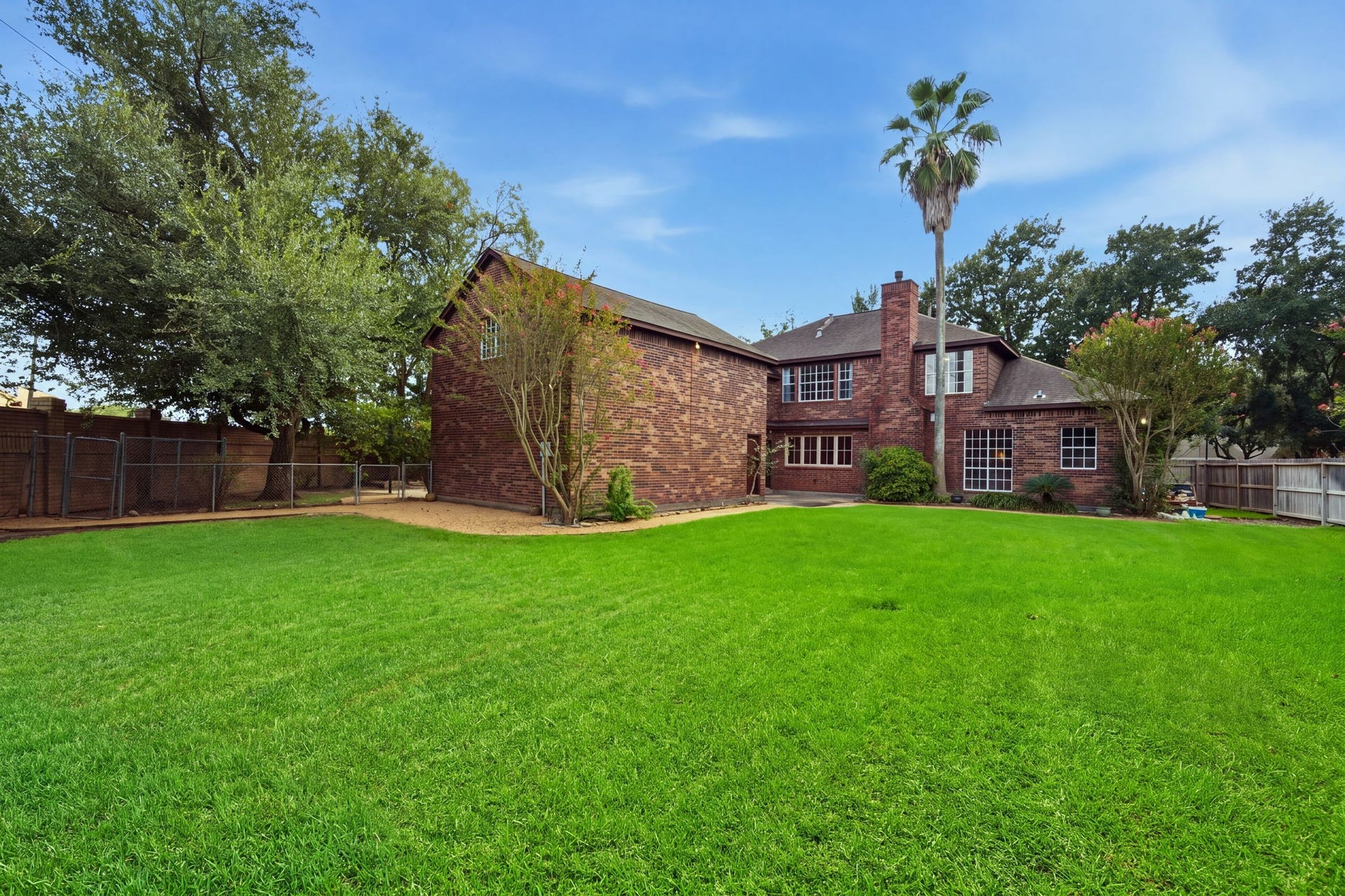Spacious backyard with lush green lawn and mature trees, complementing a charming brick home perfect for outdoor activities and relaxation.