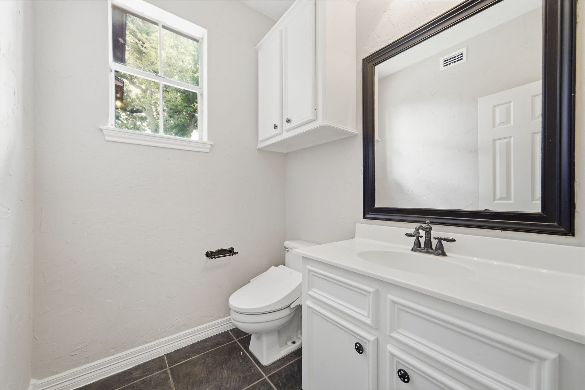 Bright guest bathroom with sleek tile flooring, a spacious vanity with a large framed mirror, and ample natural light from the window.
