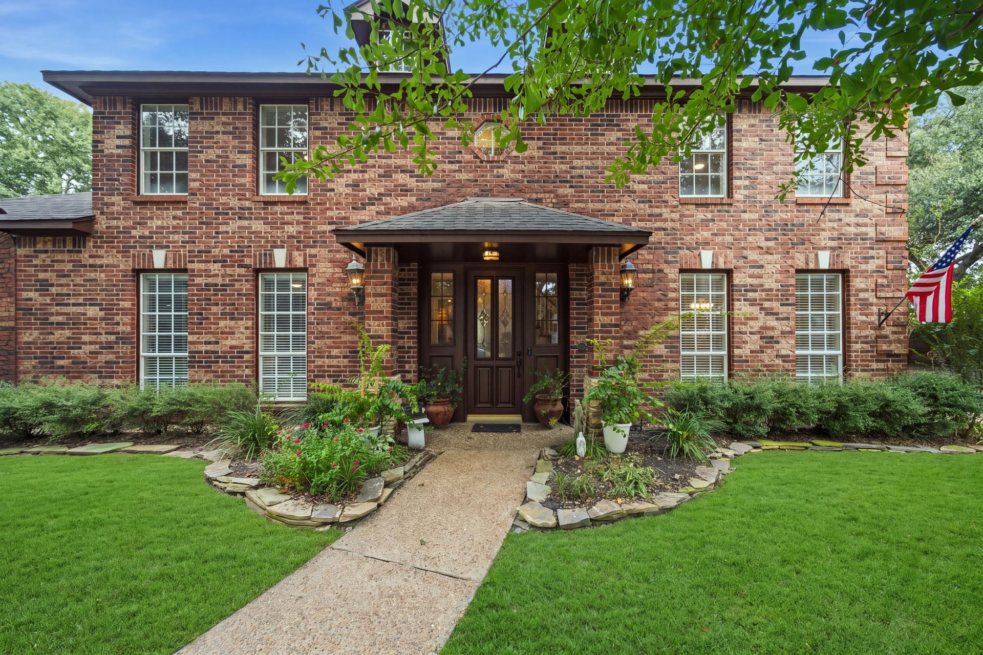 Charming two-story brick home with a welcoming front entrance, flanked by manicured landscaping and large windows that brighten the interior.