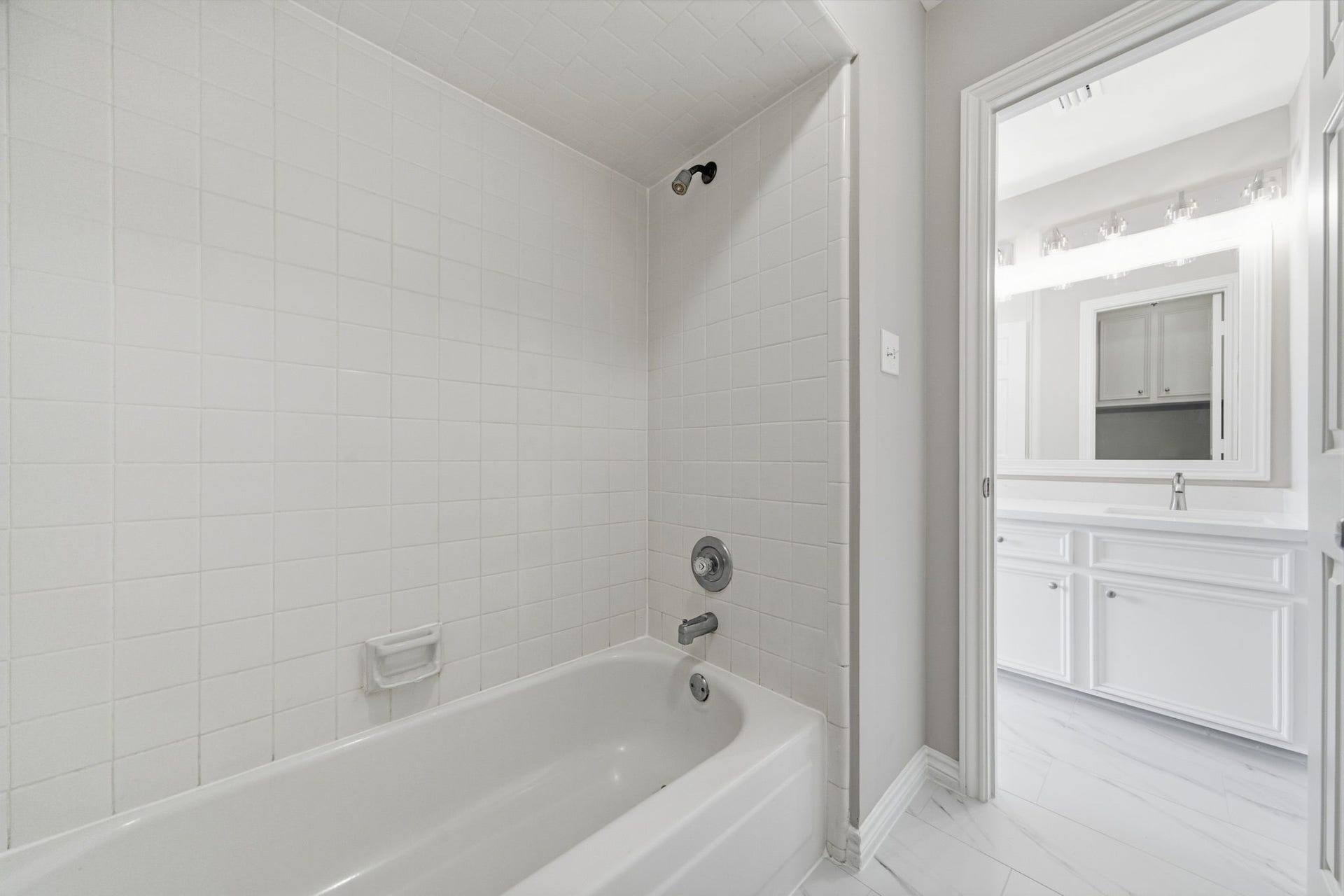 The secondary bath offers a bright vanity area with generous cabinetry and plenty of counter space for everyday routines. The adjoining tub and shower area is finished in classic white tile for a timeless look.