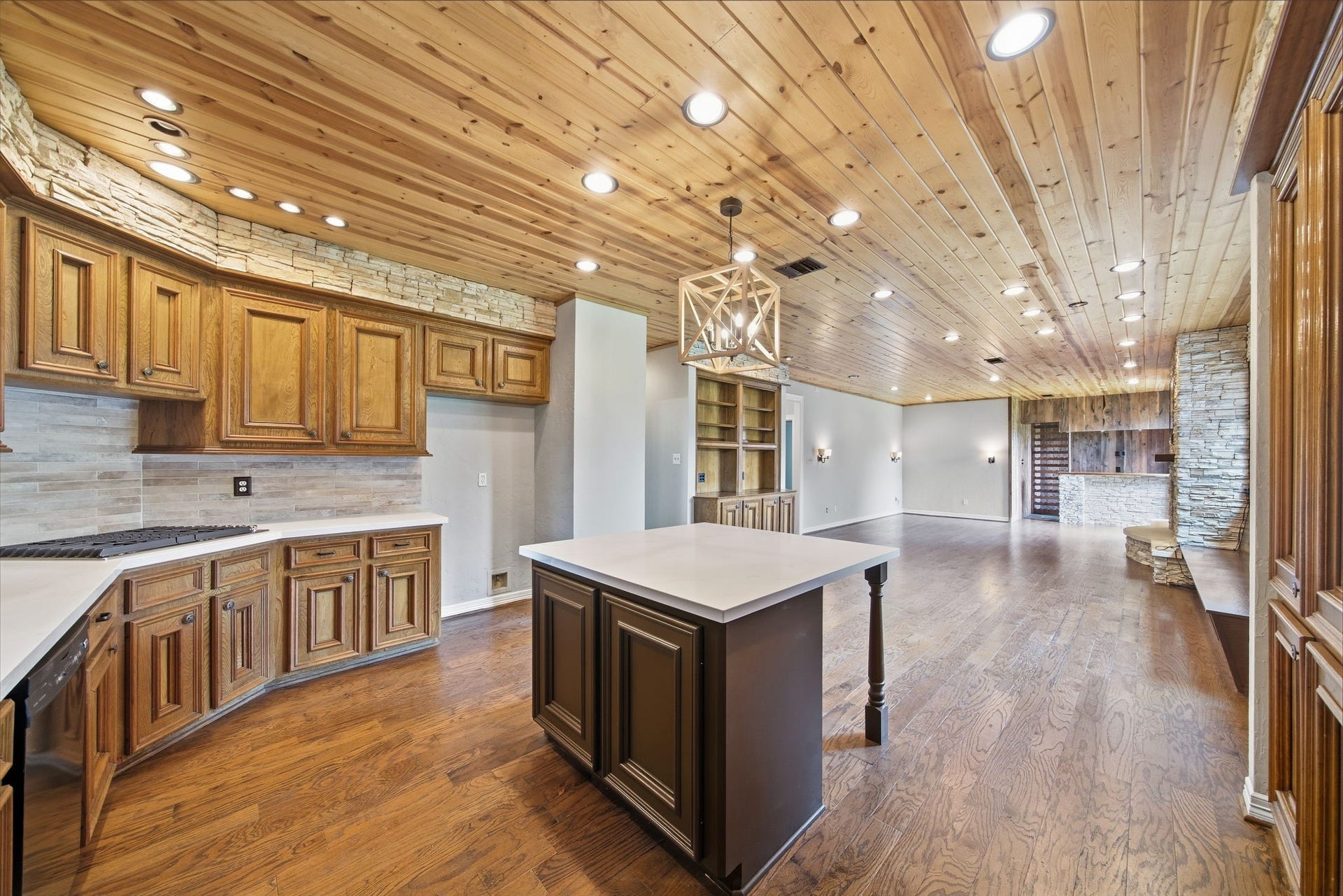 Spacious open-concept kitchen and living area featuring warm wood finishes, stone accents, and modern lighting, perfect for entertaining and family gatherings.