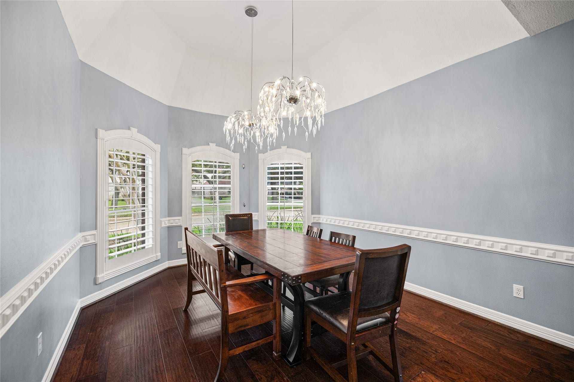 Another view of the formal dining room showcasing its dramatic ceiling height, beautiful chandeliers, and abundant natural light through three arched windows.