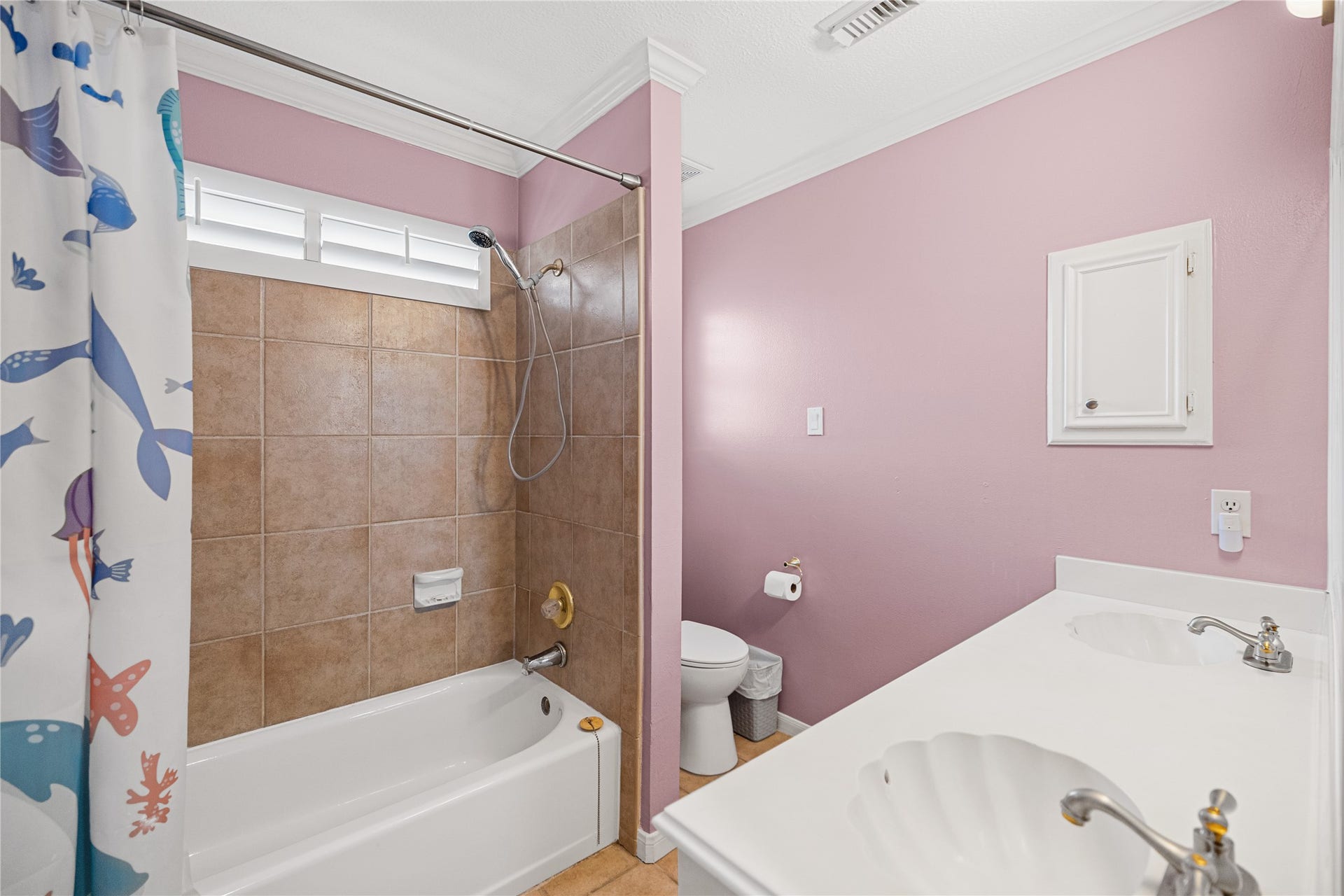 Secondary bathroom featuring double sinks, a tub/shower combination with tile surround, and convenient vanity space.