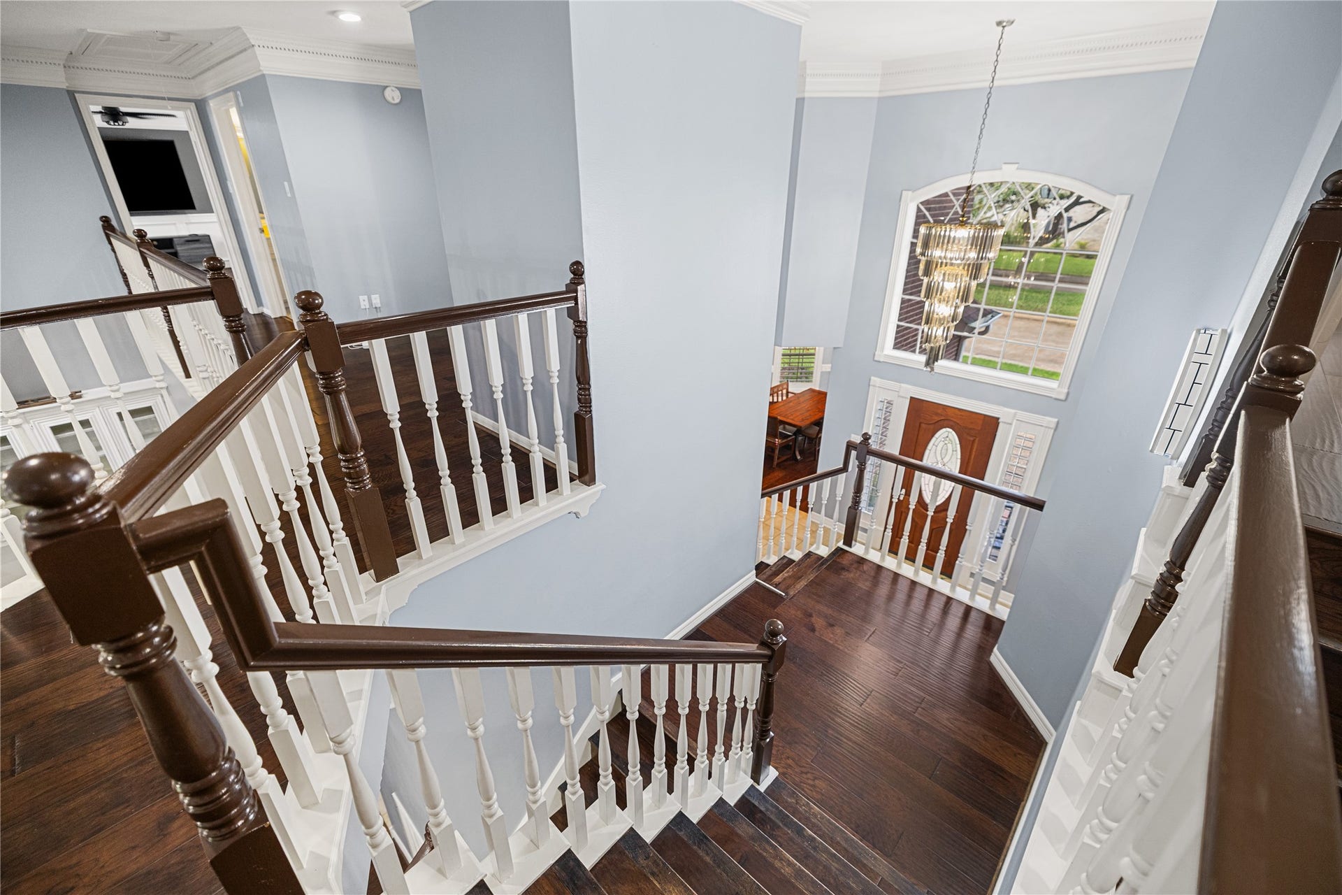 Beautiful staircase with wood treads, contrasting railings, and an elegant two-story foyer featuring a large arched window and statement chandelier.