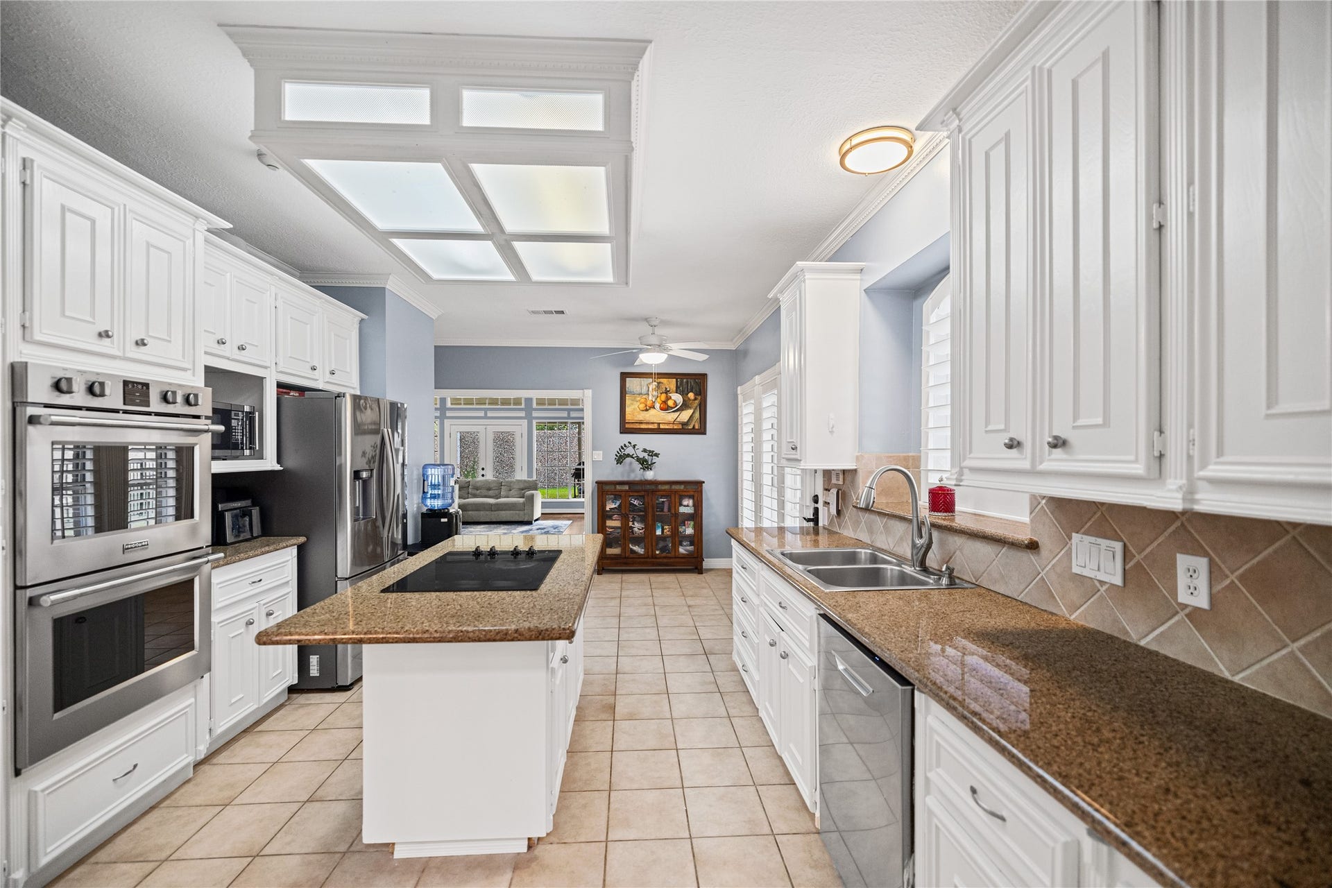 Spacious kitchen featuring white cabinetry, Silestone countertops, center island with electric cooktop, double ovens, and adjoining breakfast area.