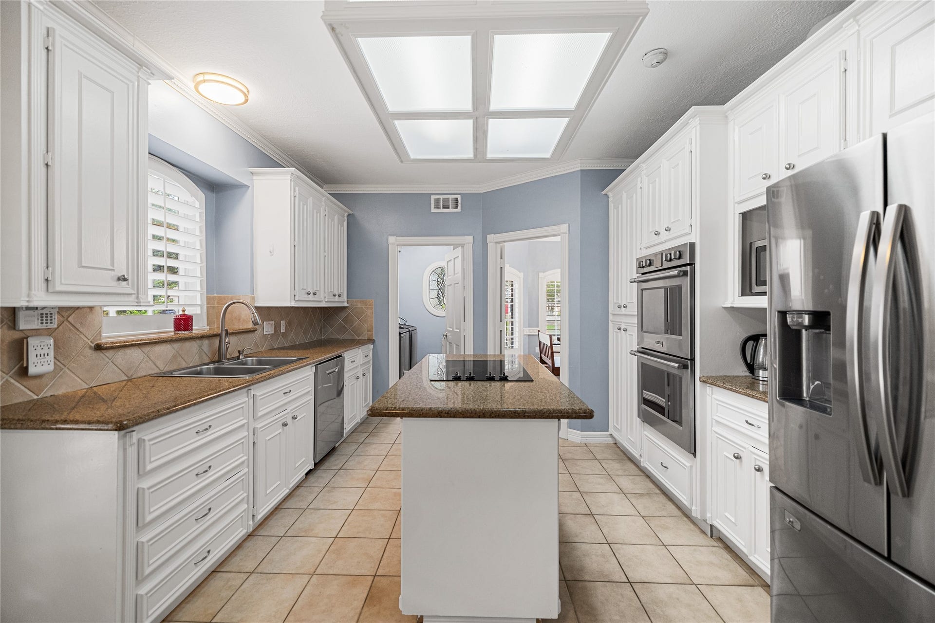Spacious kitchen featuring white cabinetry, Silestone countertops, center island with electric cooktop, double ovens, and stainless steel appliances.