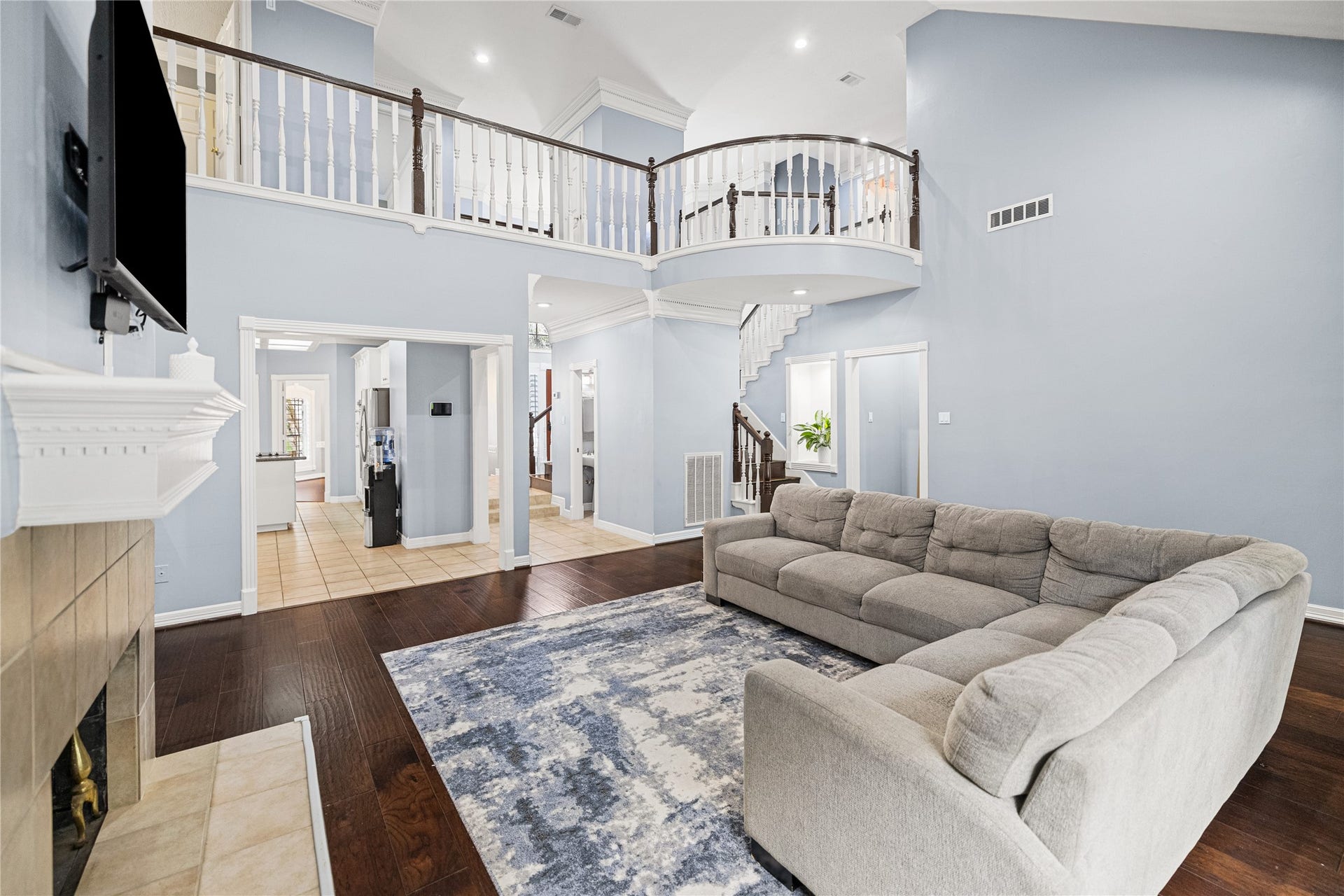 Impressive two-story family room featuring soaring ceilings, engineered wood flooring, gas-log fireplace, and elegant curved upstairs balcony.