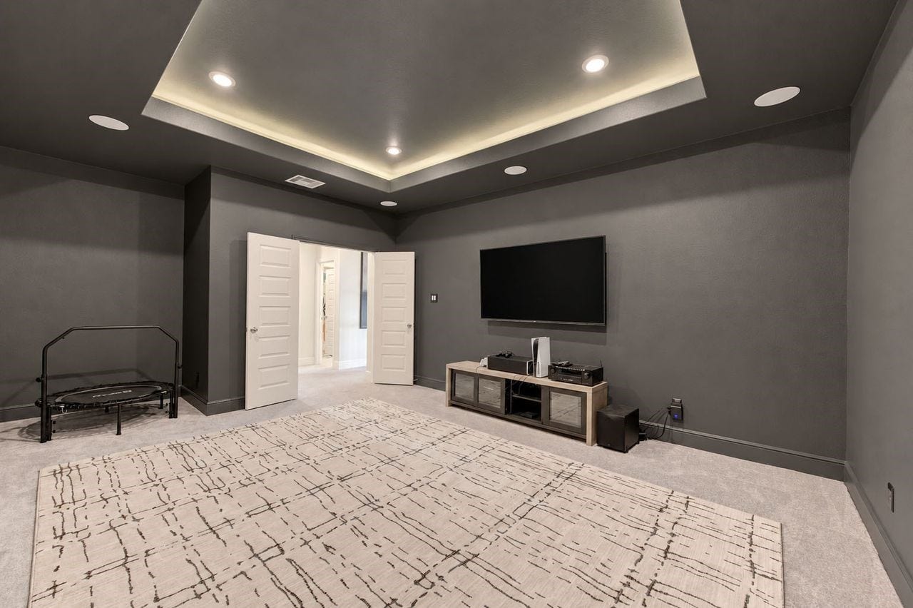 2803 Enriched Enclave Court, Richmond, TX 77406 Spacious dedicated media room featuring a dramatic tray ceiling with ambient lighting, recessed lighting, built-in surround sound, and a dark theater-inspired color paletteperfect for movie nights, gaming, and entertaining.