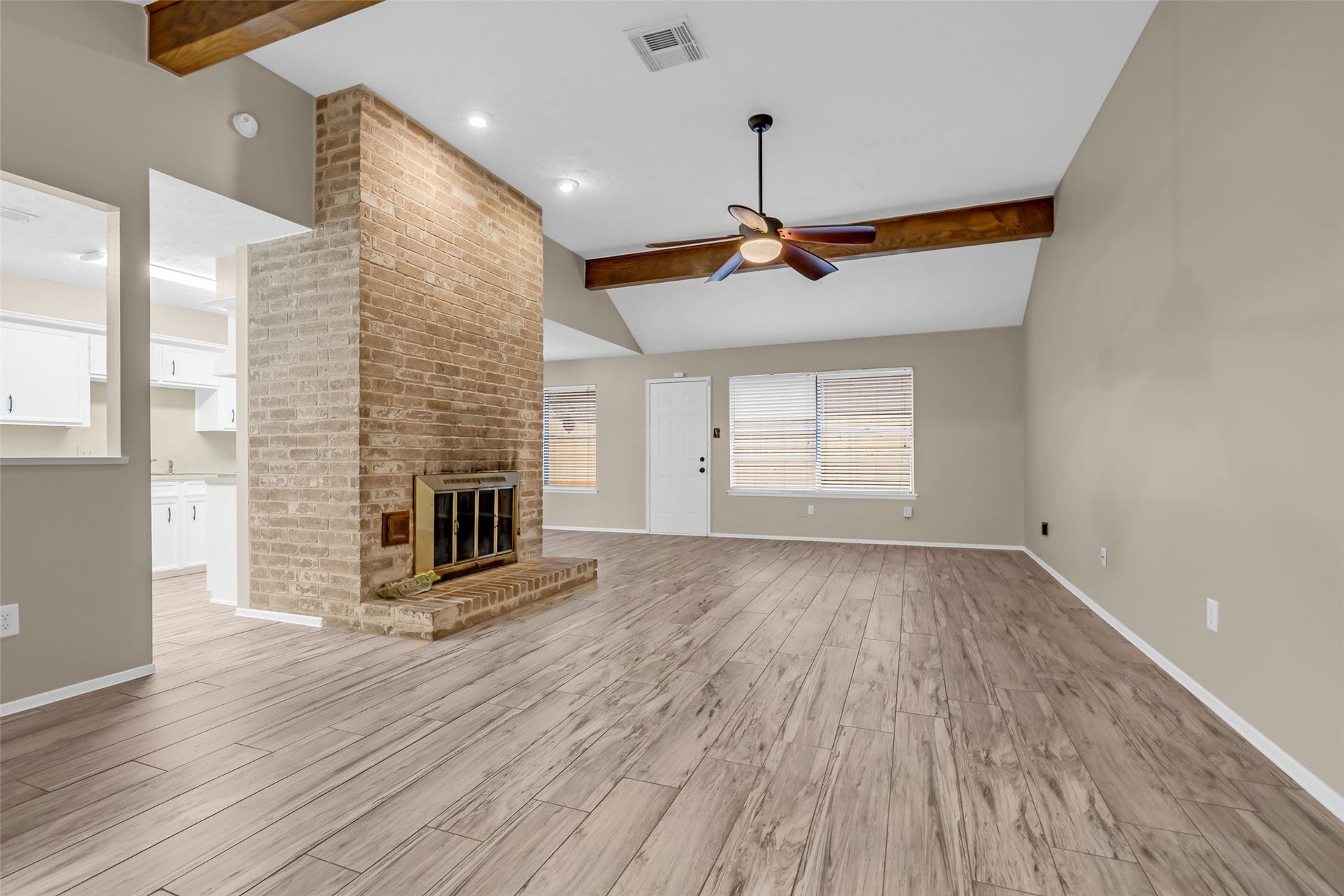 11827 Brook Meadows Lane, Meadows Place, TX 77477 This spacious living room features a vaulted ceiling with exposed wooden beams, a central brick fireplace, and tile flooring. Natural light fills the space through large windows, and an open doorway leads to the kitchen area.
