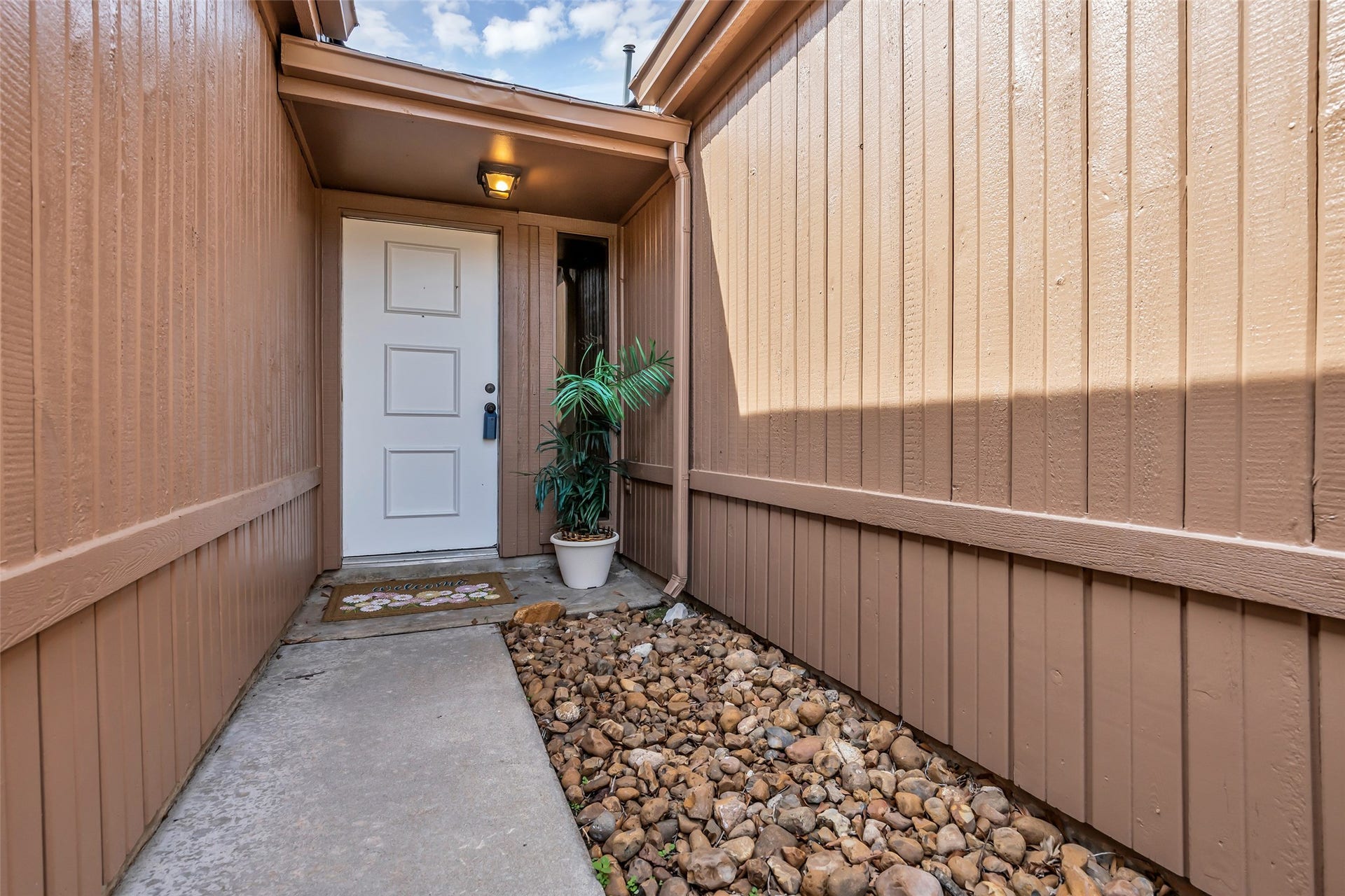 11827 Brook Meadows Lane, Meadows Place, TX 77477 Cozy entryway lined with stones leads to a covered porch, featuring wood paneling and a welcoming front entrance