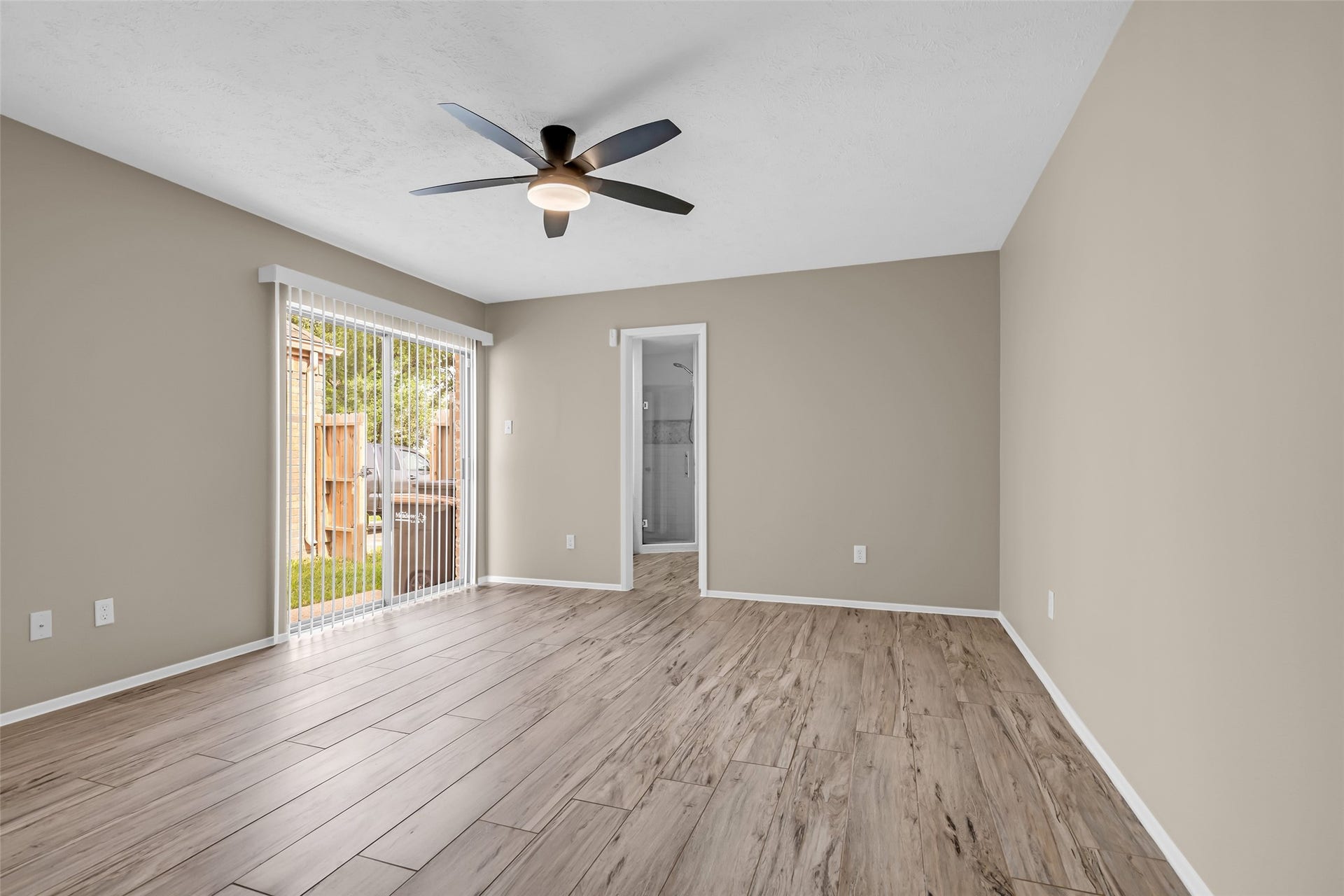 11827 Brook Meadows Lane, Meadows Place, TX 77477 The Primary Bedroom features wood-look tile flooring, neutral wall colors, and a modern ceiling fan. It has large sliding glass doors leading to the side and back yard, offering natural light and outdoor access. The space is versatile and inviting.