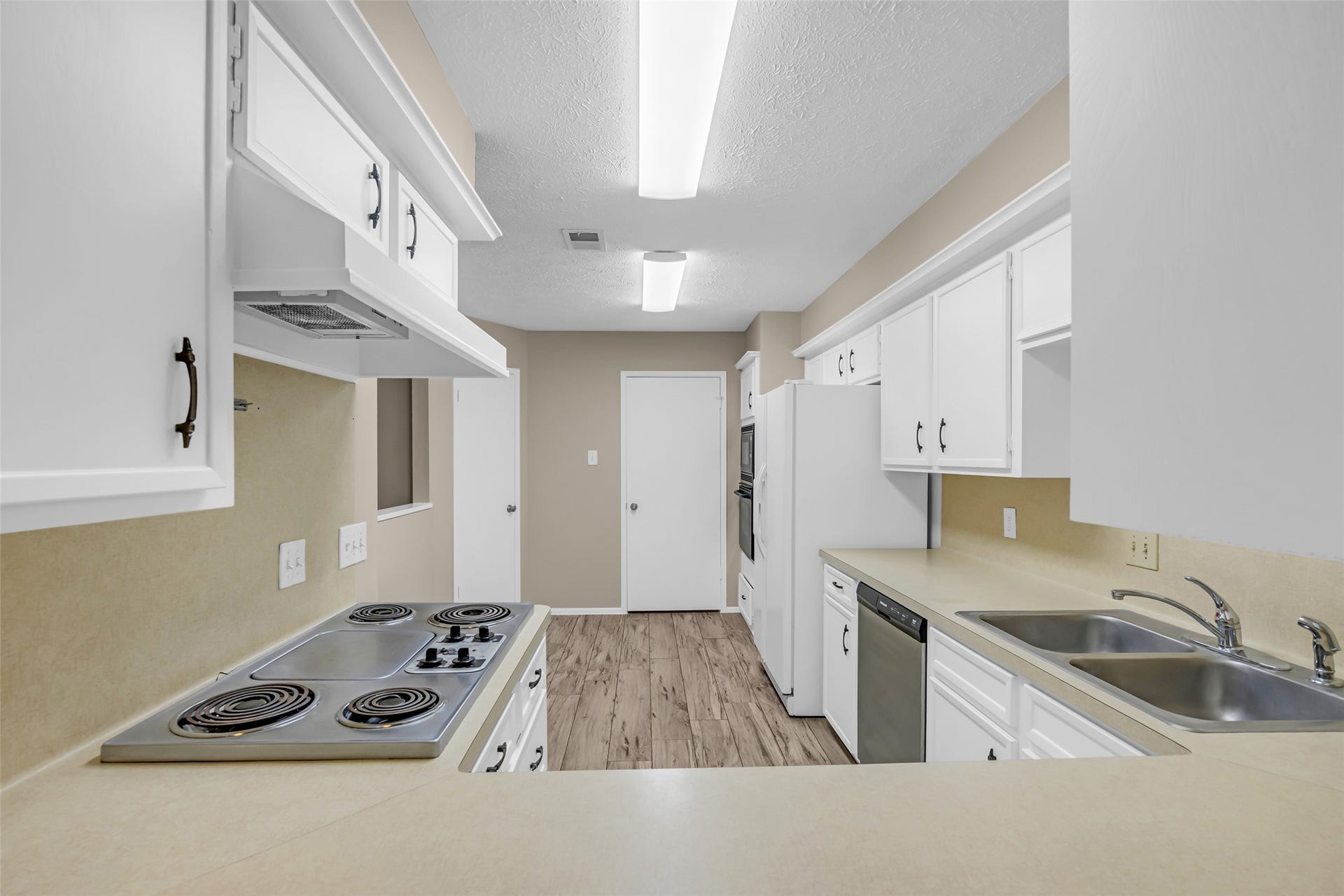 11827 Brook Meadows Lane, Meadows Place, TX 77477 Bright and spacious kitchen with new fluorescent lights, featuring white cabinetry, a dual sink, electric cooktop, and modern appliances. The neutral countertops and wood-style flooring add a warm touch.