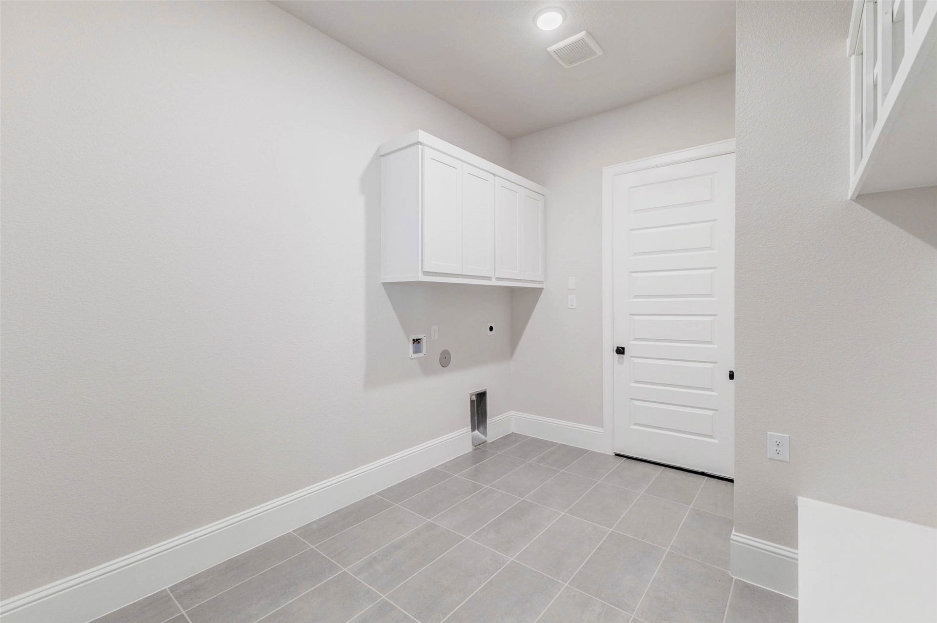 Spacious laundry room with tile flooring, white cabinetry, and utility hookups.