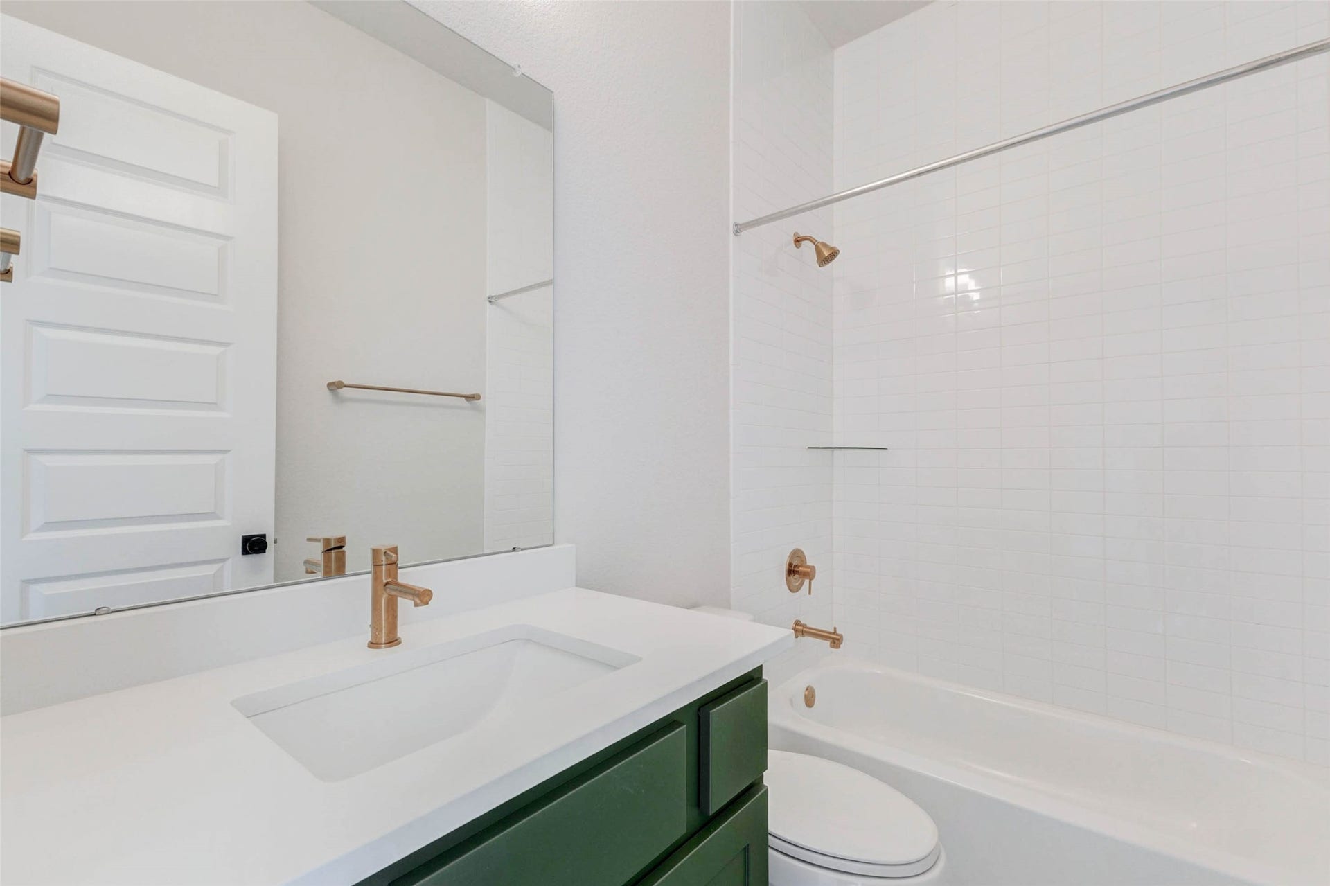 This bathroom features a clean, modern design with a white countertop, green vanity, and elegant gold fixtures. It includes a full bathtub/shower combo with tile to the ceiling.