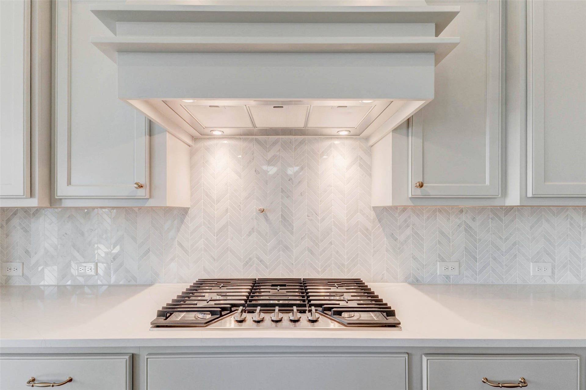 Sleek gas cooktop with a stylish herringbone tile backsplash.