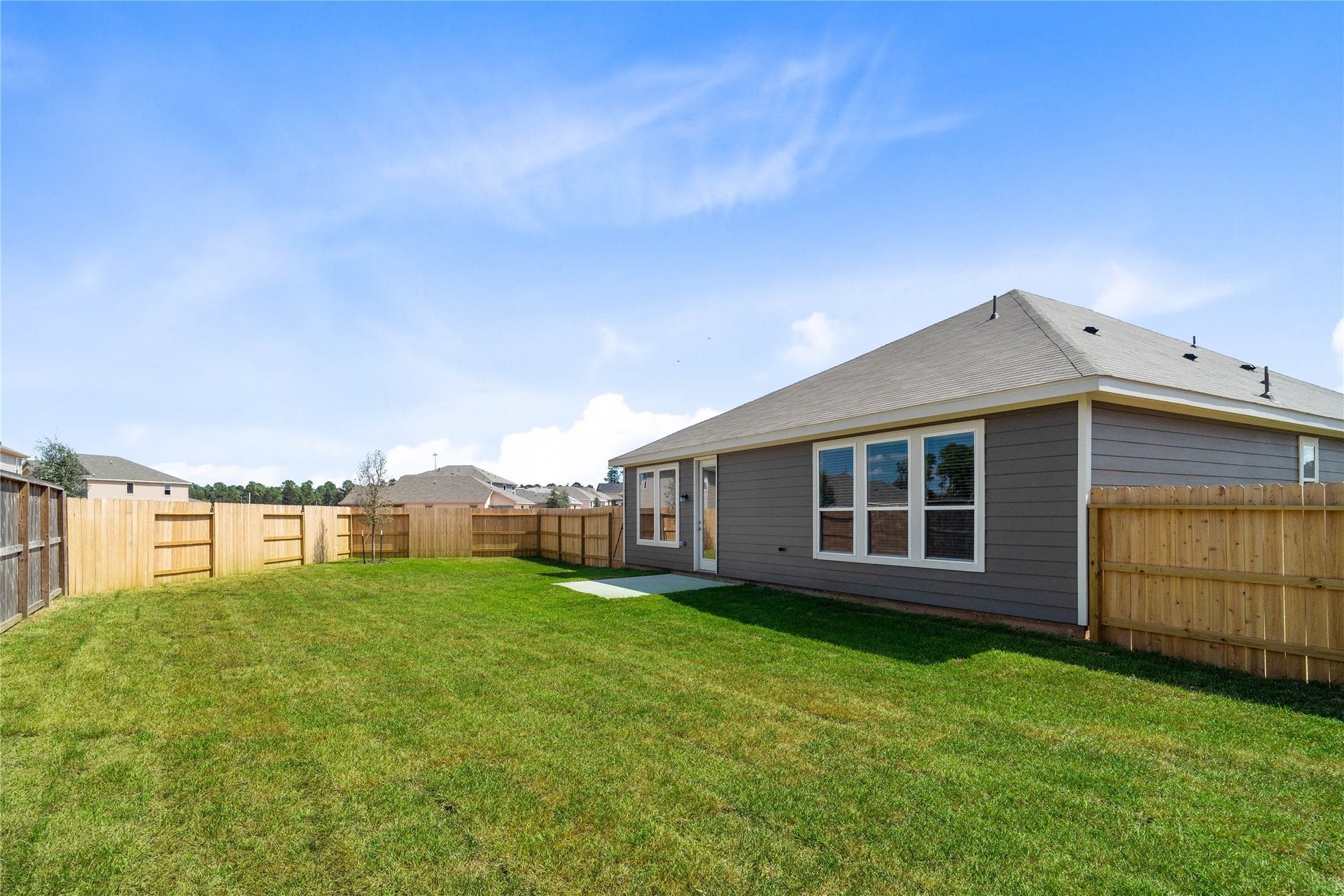 A spacious green backyard featuring a freshly manicured lawn enclosed by a wooden privacy fence.