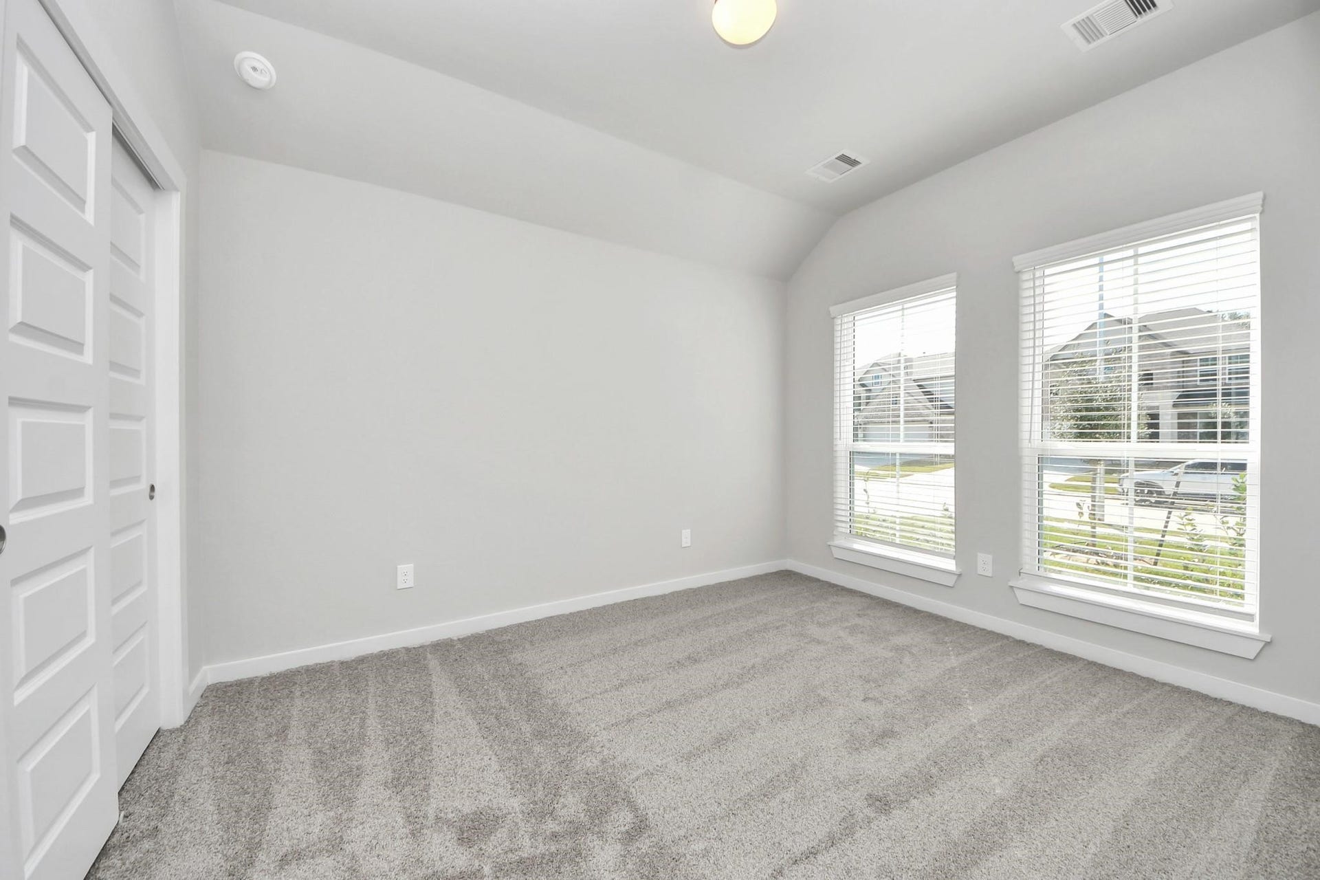 Bright and airy room with large windows, plush carpeting, and a spacious double-door closet, perfect for a cozy retreat or home office.
