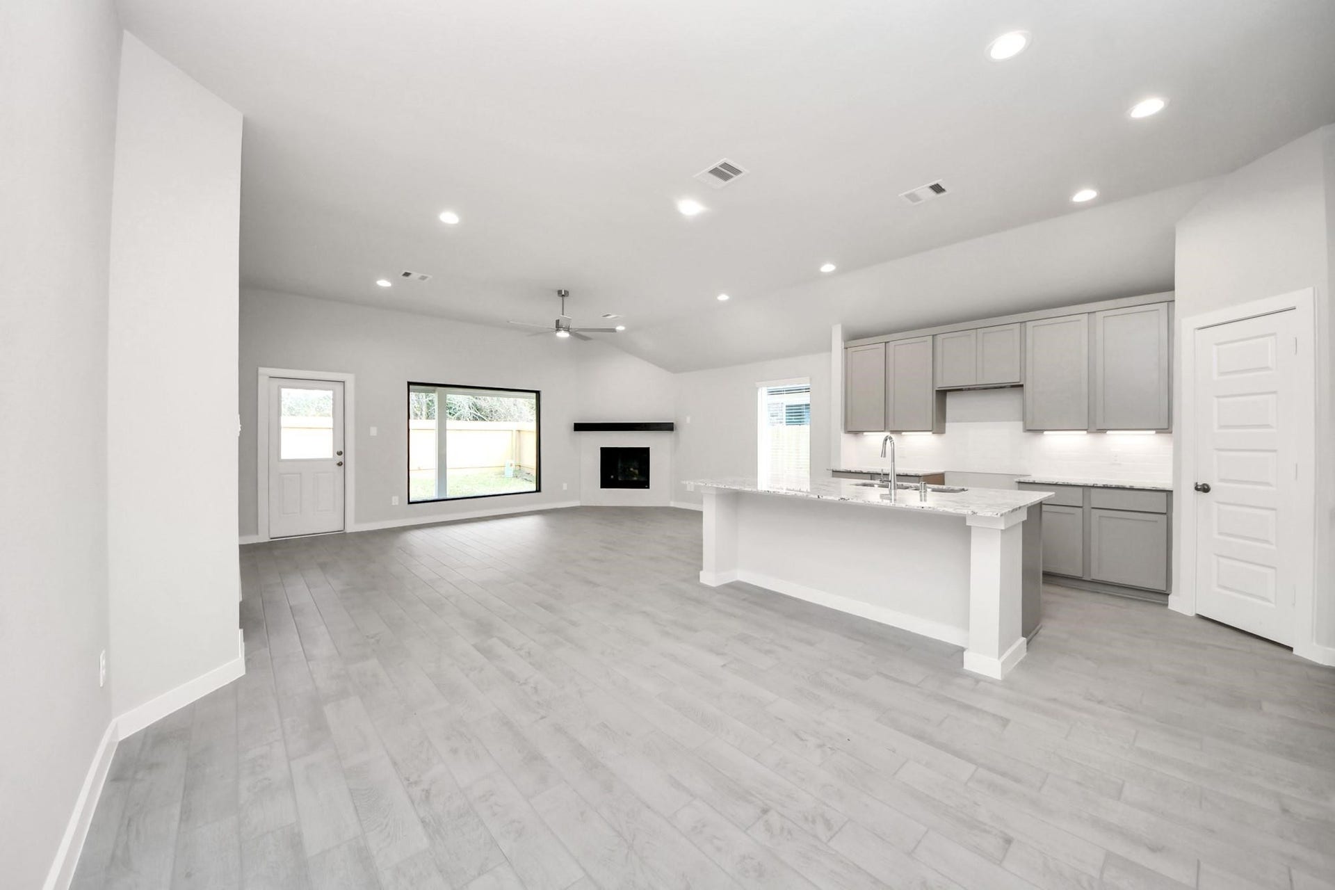 Spacious open-concept living area with sleek hardwood floors, modern kitchen featuring an island with bar seating, and a cozy fireplace under a vaulted ceiling.