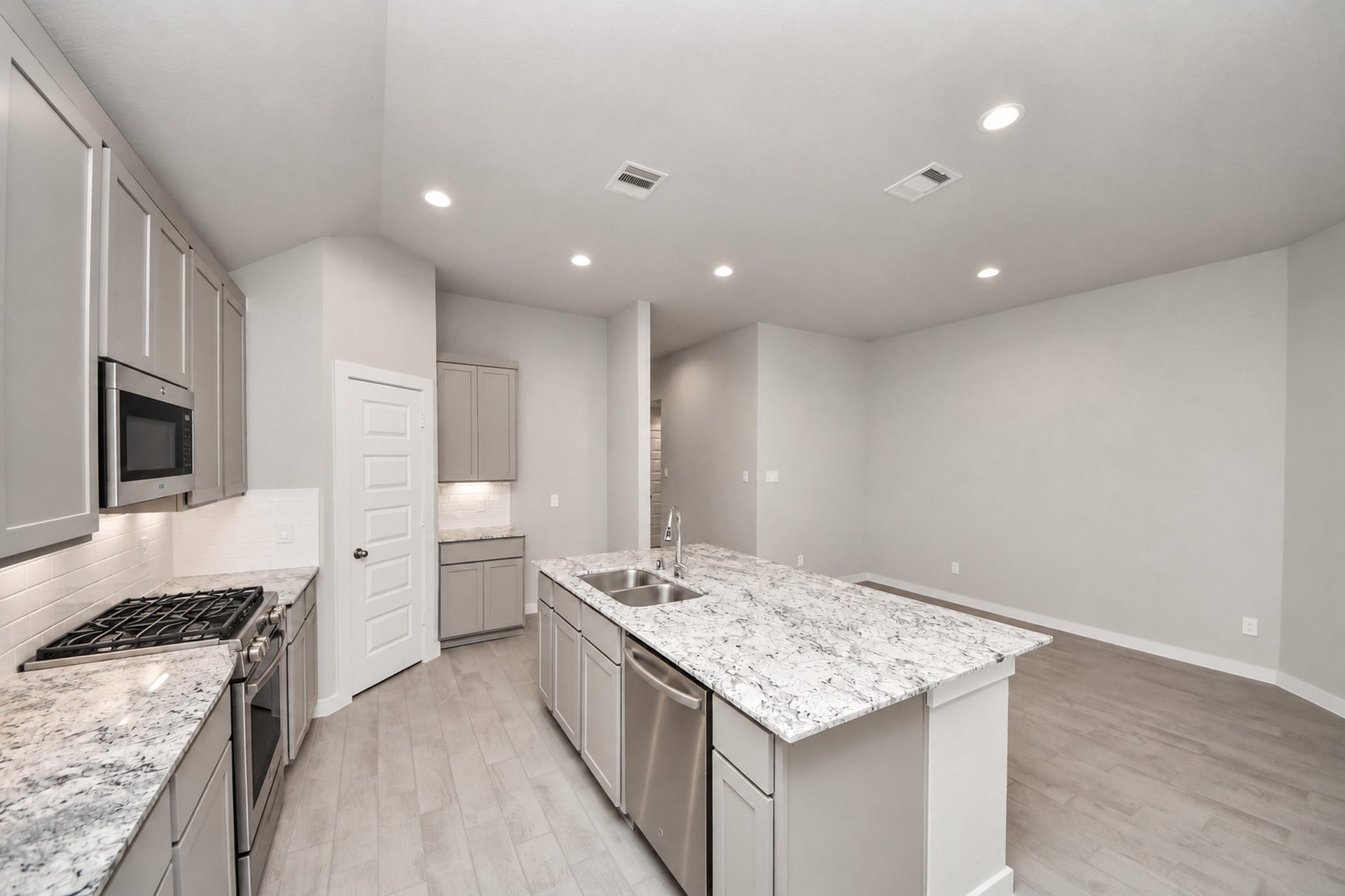 Modern kitchen featuring sleek granite countertops, stainless steel appliances, and ample cabinetry, seamlessly flowing into a spacious open-concept living area.