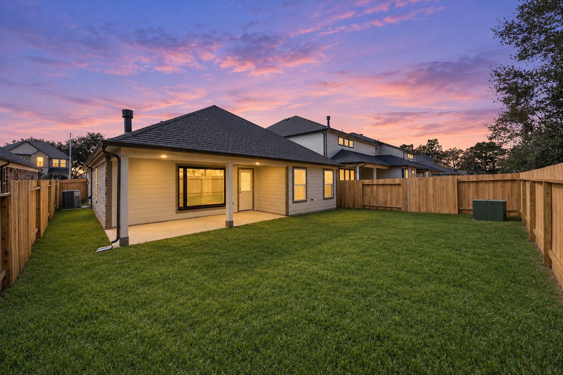Charming backyard with a spacious lawn and a cozy covered patio, perfect for outdoor relaxation and entertaining, all set against a stunning sunset backdrop.