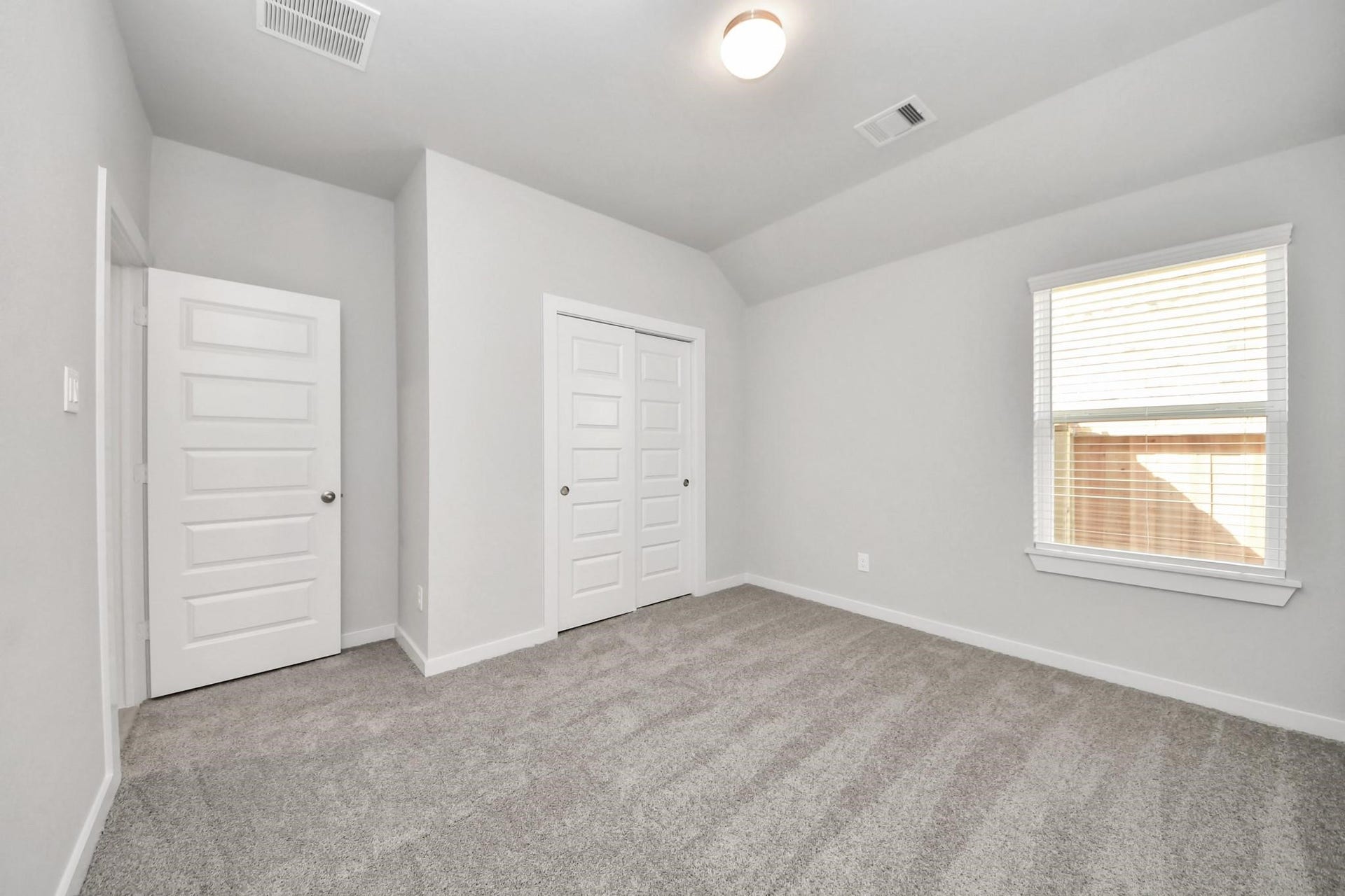 Bright and airy bedroom featuring plush carpeting, dual closet doors, and a large window for natural light.