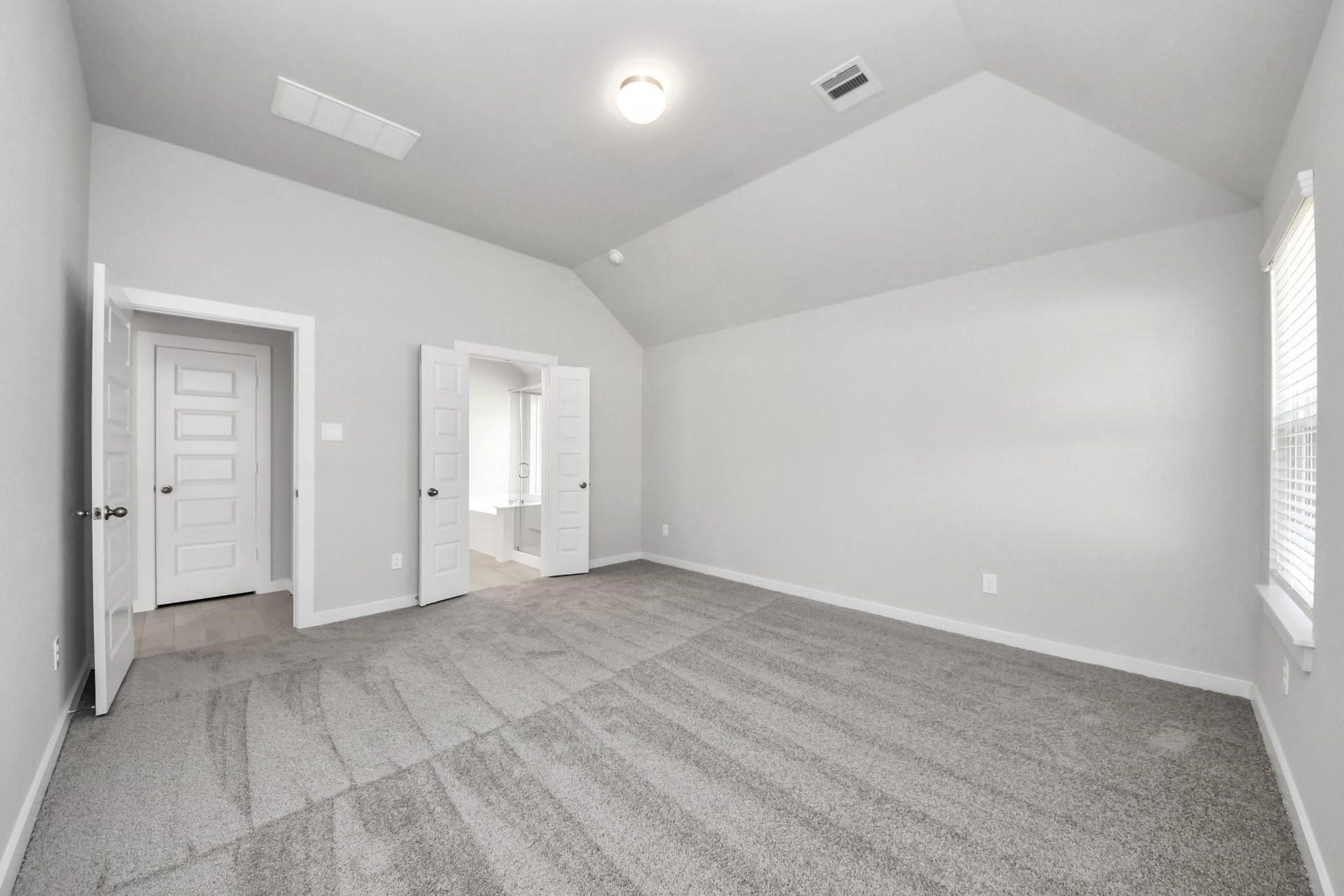 Spacious bedroom with vaulted ceilings, soft carpet flooring, and ample natural light from a large window, offering a serene retreat.