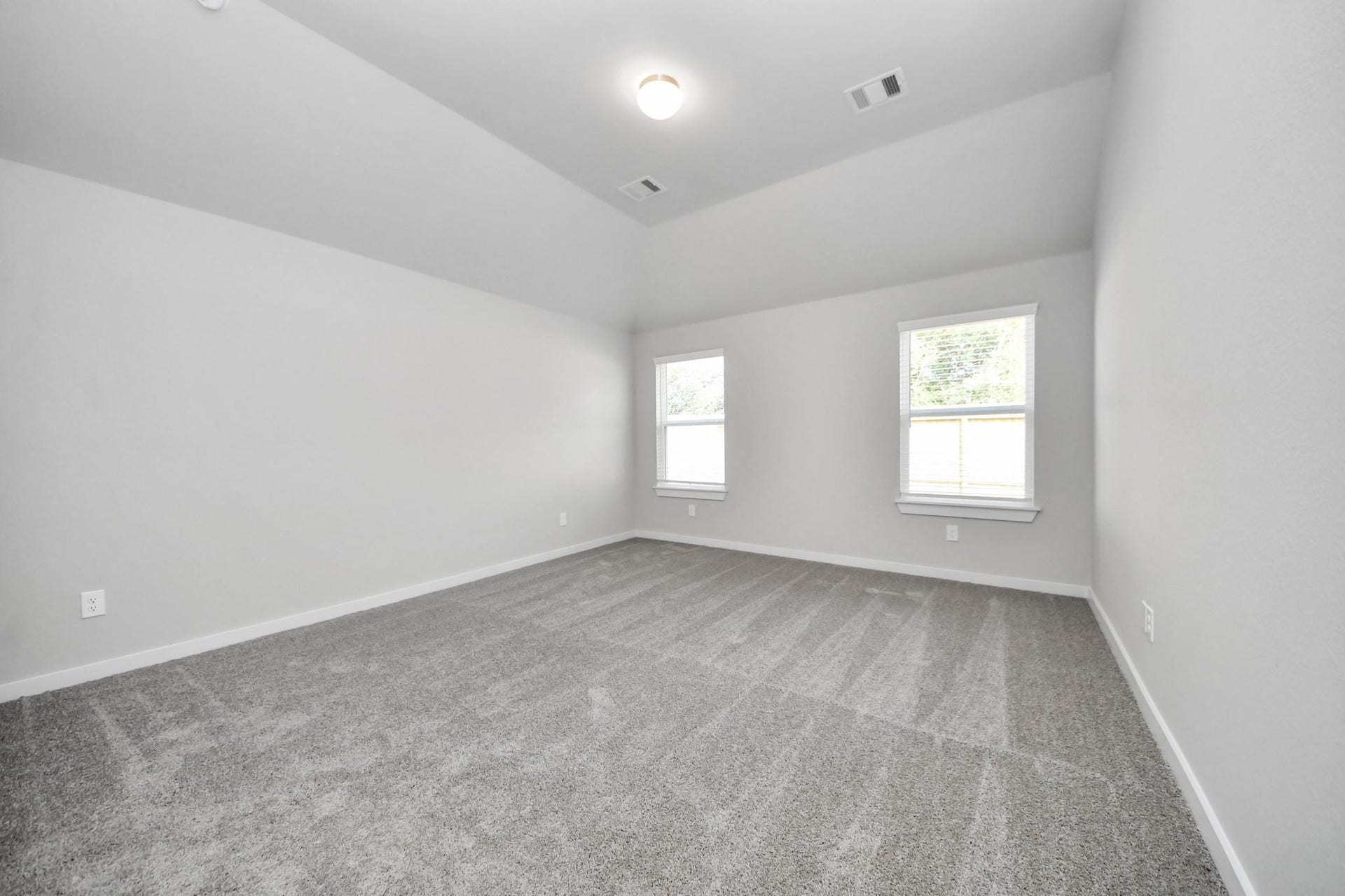 Spacious and bright room with plush carpeting and high ceilings, featuring two large windows that let in ample natural light.