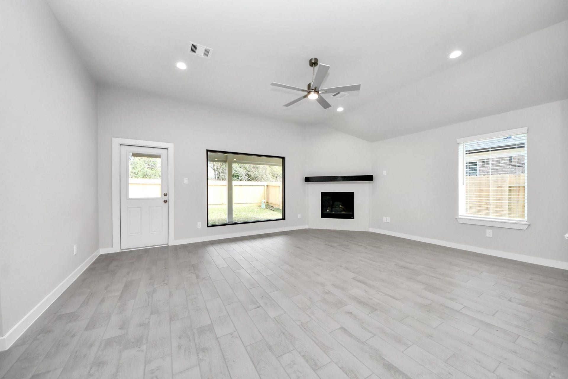 Spacious living room with modern gray flooring, a sleek corner fireplace, and large windows offering ample natural light.