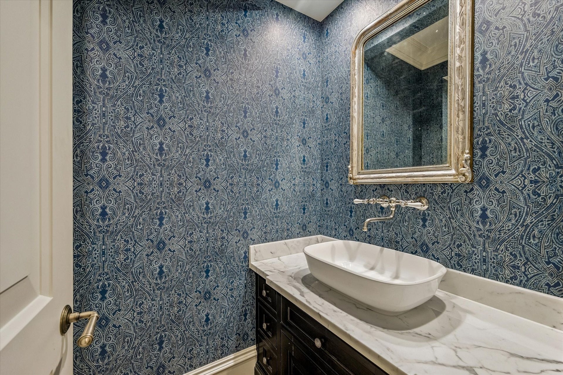 2158 Chilton Road, Houston, TX 77019 The game room powder room is richly appointed with designer wallpaper, Alkusari stone tile flooring, and elegant marble countertops. A ceramic vessel sink paired with a vintage-inspired wall-mounted faucet creates a distinctive focal point, while thoughtful storage and premium fixtures complete the sophisticated space.