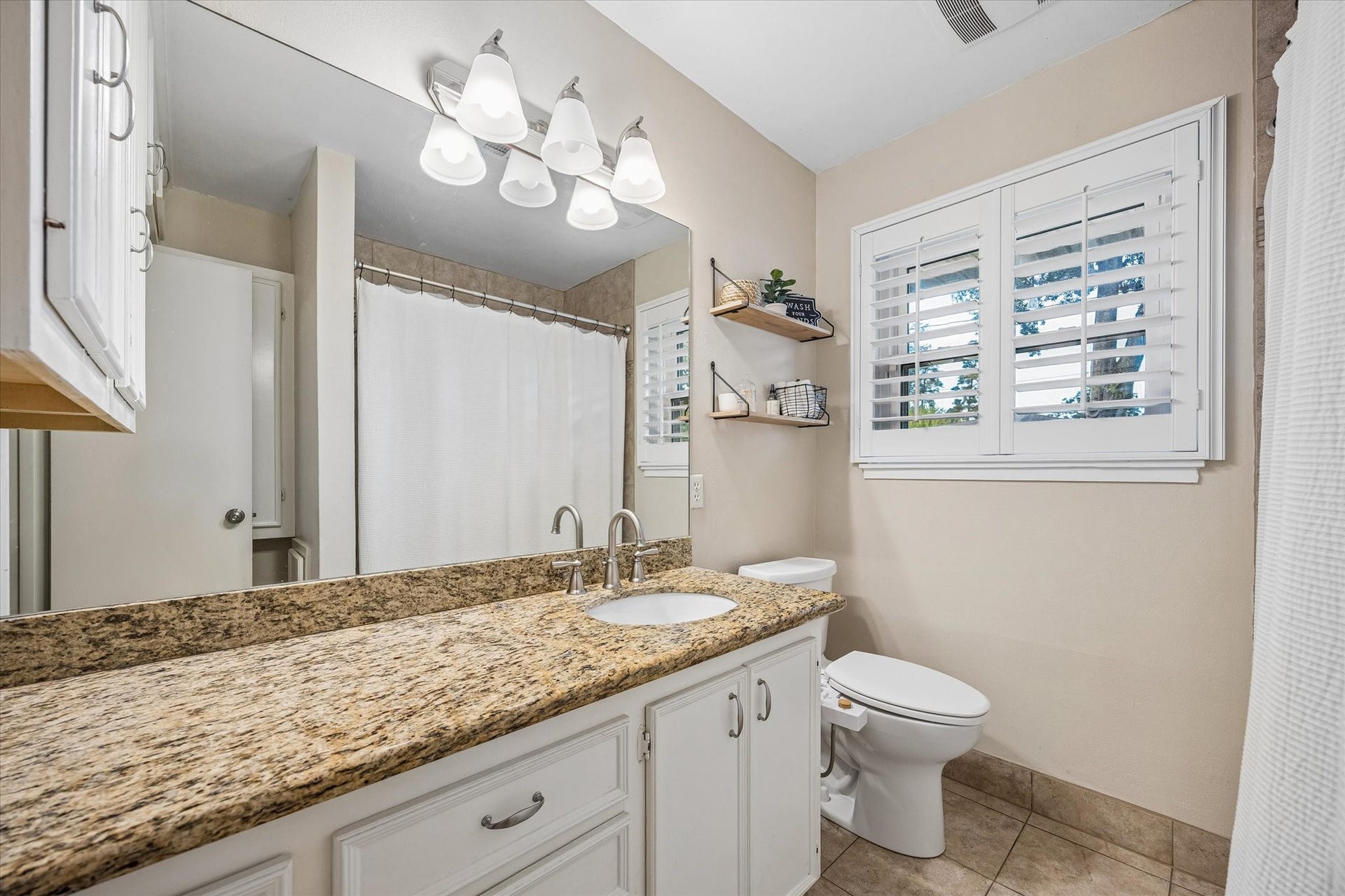 2318 Cheshire Lane, Houston, TX 77018 Wide vanity counter provides room for daily routines, with cabinet storage below to keep essentials organized. A shuttered window brings natural light and privacy control to the bathroom near the bedrooms.