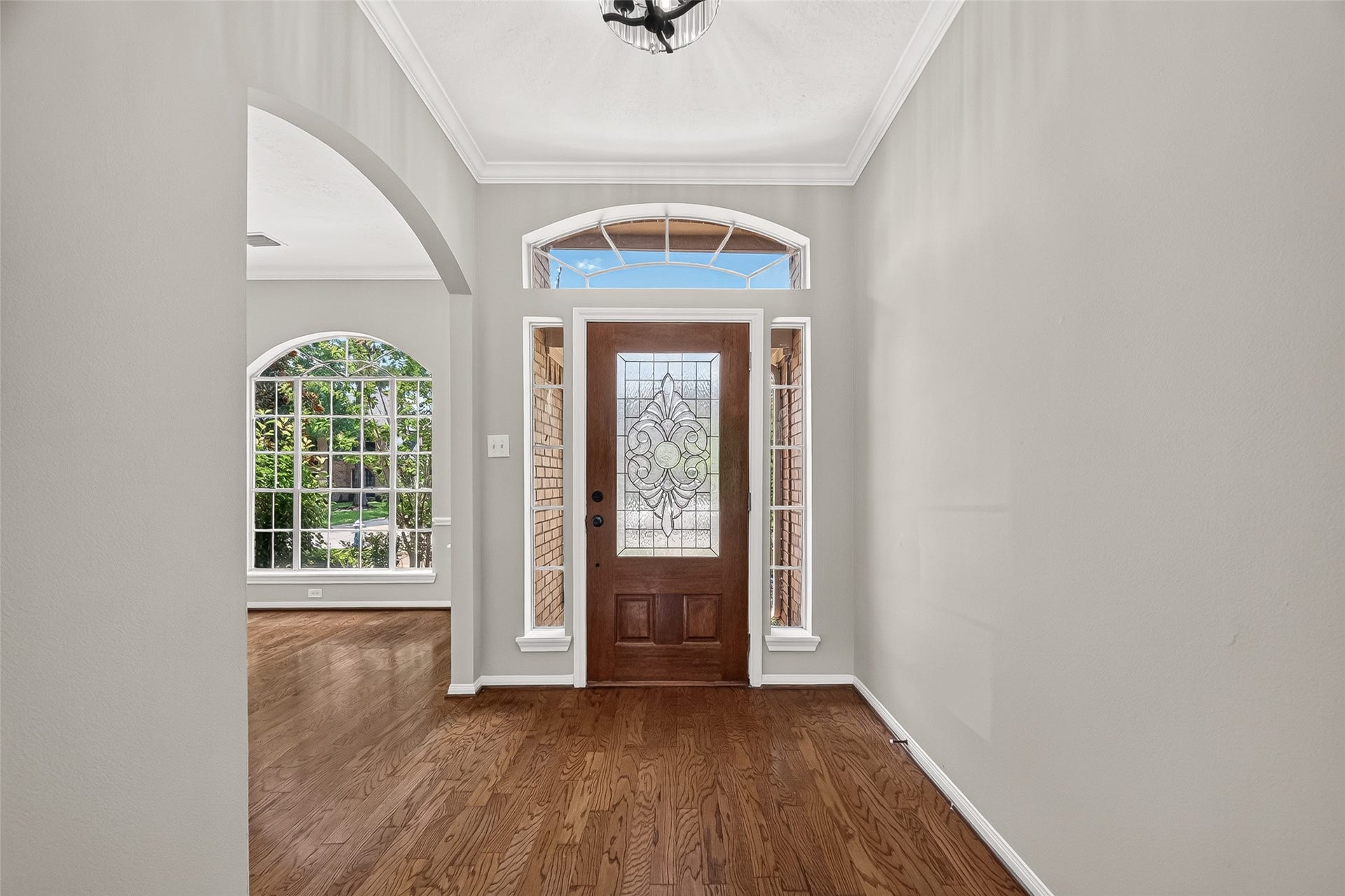 12823 Lady Jane Court, Houston, TX 77044 Entryway with a beautifully detailed wooden door and sidelights, complemented by rich hardwood flooring and abundant natural light from large arched windows.