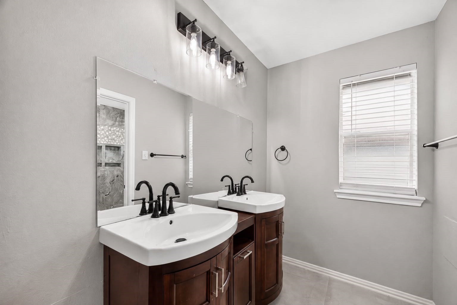 12823 Lady Jane Court, Houston, TX 77044 Modern bathroom featuring a double sink vanity with elegant dark wood cabinets, sleek fixtures, and a large mirror, complemented by a soft gray color palette and ample natural light.