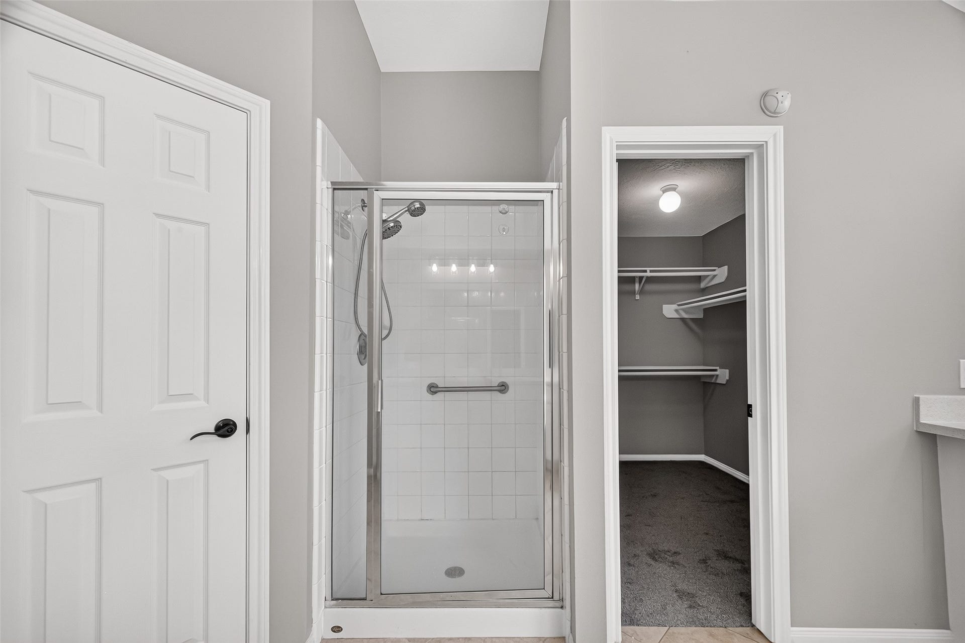 12823 Lady Jane Court, Houston, TX 77044 A sleek, modern bathroom features a glass-enclosed shower alongside a spacious walk-in closet with ample shelving, all set against elegant, neutral tones.