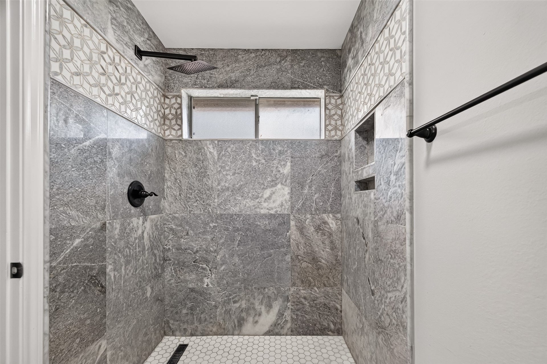 12823 Lady Jane Court, Houston, TX 77044 Luxurious bathroom featuring elegant gray marble tiles, a stylish geometric accent strip, and a modern rainfall showerhead for a spa-like experience.