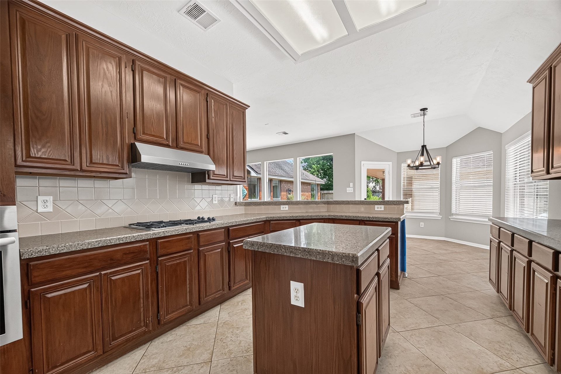 12823 Lady Jane Court, Houston, TX 77044 Spacious kitchen with rich wood cabinetry, granite countertops, and a central island. Ample natural light fills the room, highlighting the tile flooring and open layout, perfect for gatherings.