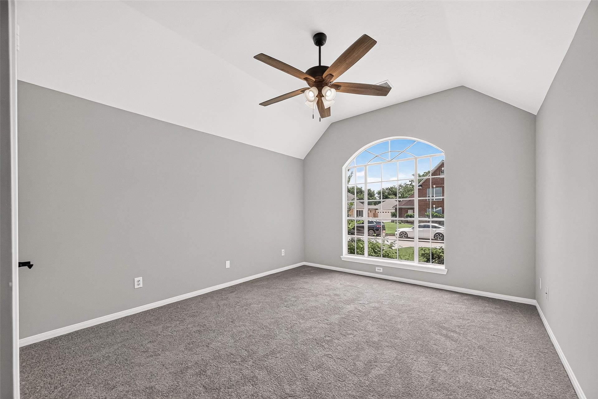 12823 Lady Jane Court, Houston, TX 77044 Spacious, light-filled room featuring a vaulted ceiling, elegant fan, and a large arched window overlooking the neighborhood.